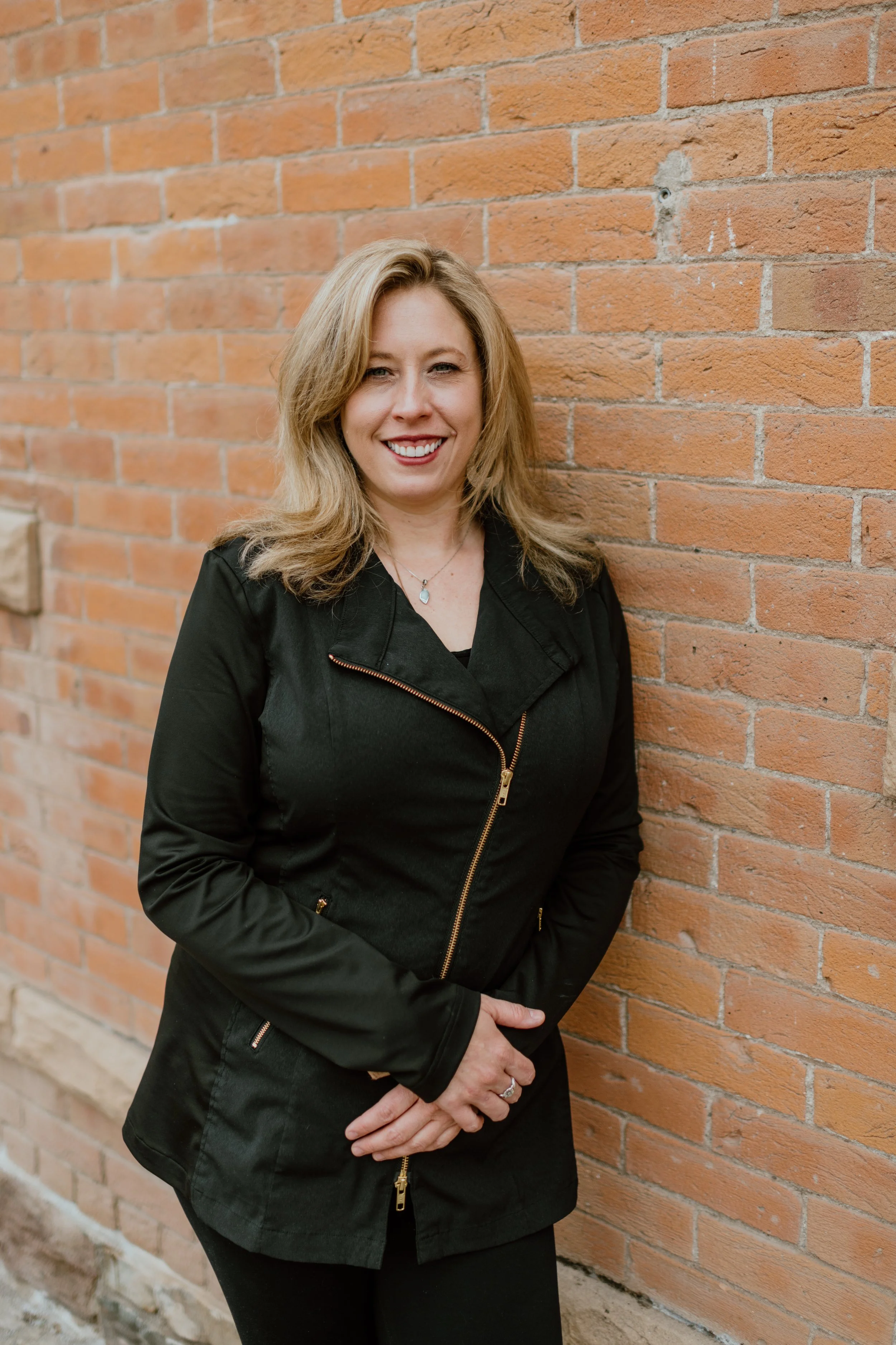 Mandy Simpson licensed massage therapist and cosmetologist leaning against a brick wall in Bozeman Montana