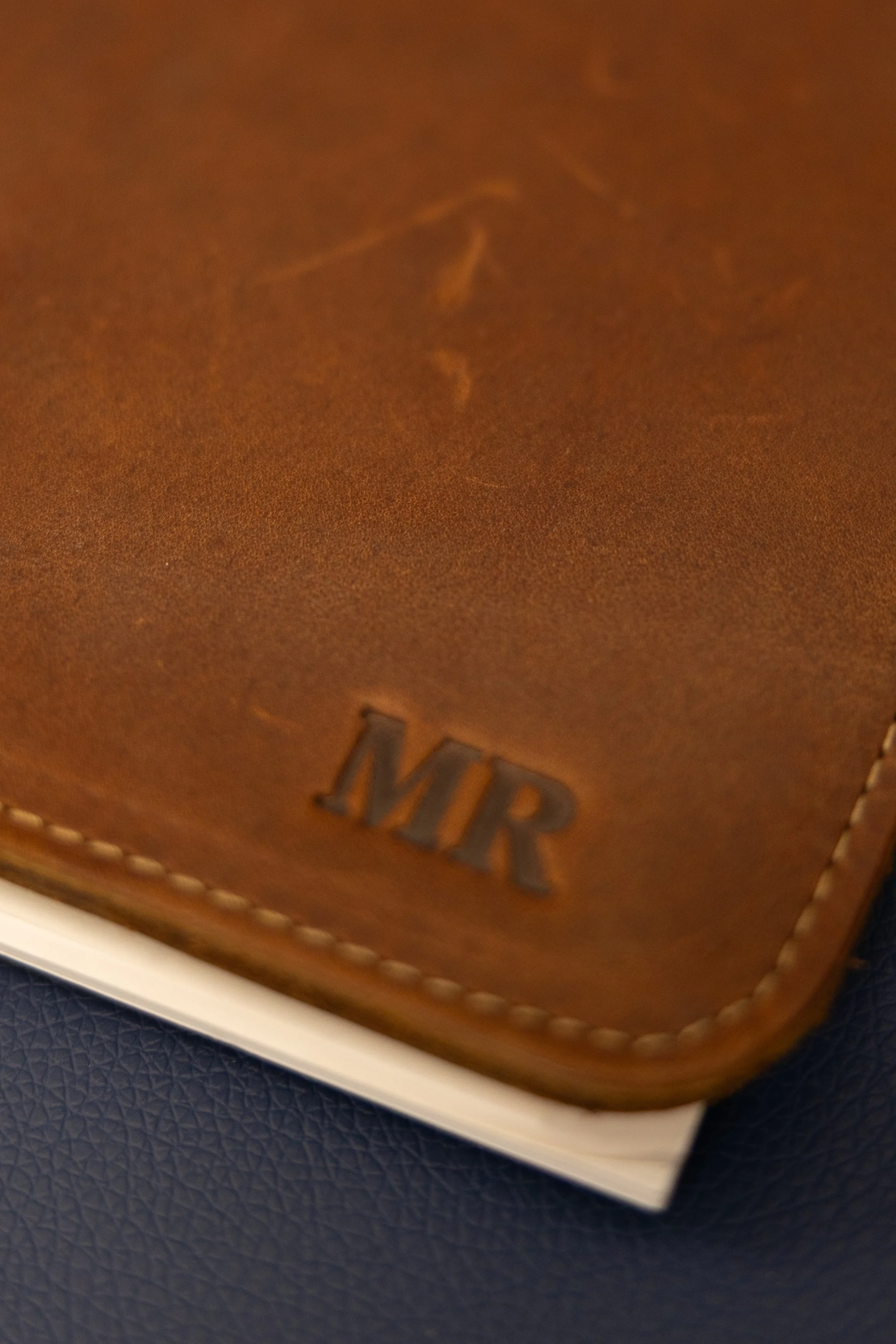 Close-up of a brown leather box with the word "BURY" embossed on it, placed on a dark textured surface.