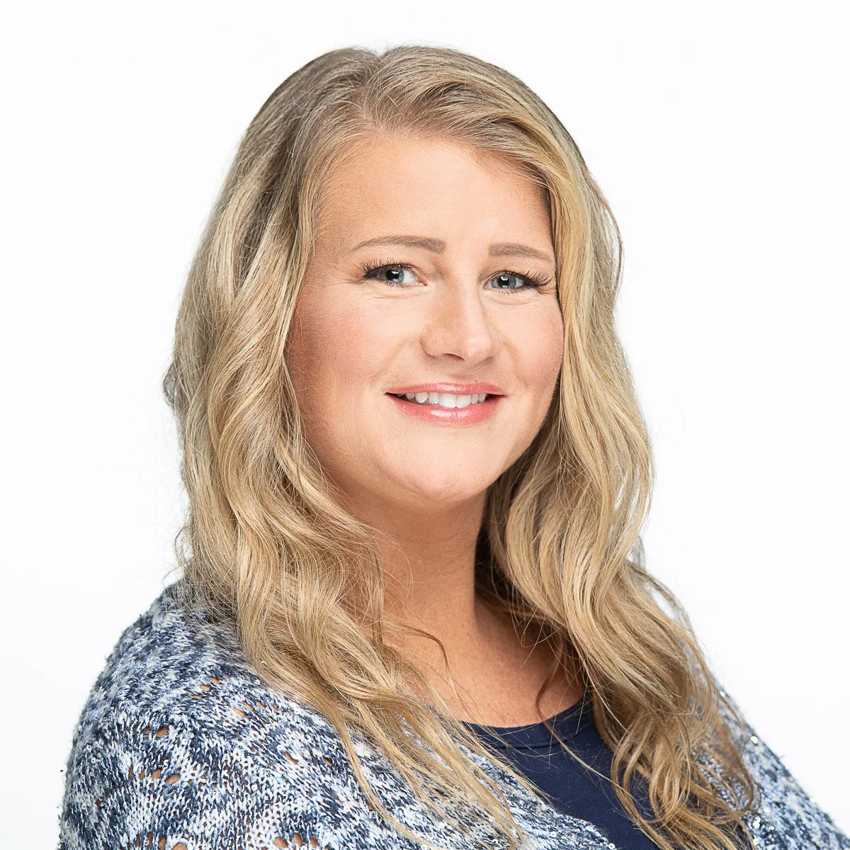 Portrait of a woman with blonde wavy hair, blue eyes, and a bright smile, wearing a patterned top.