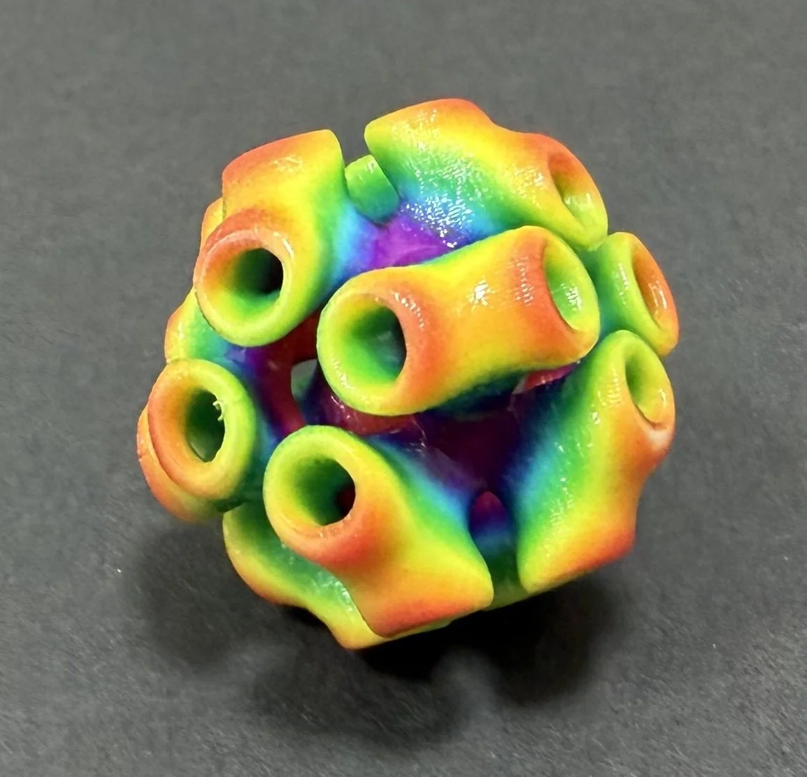 Colorful geometric object with rainbow pattern and hollow circular openings, resting on a dark surface.