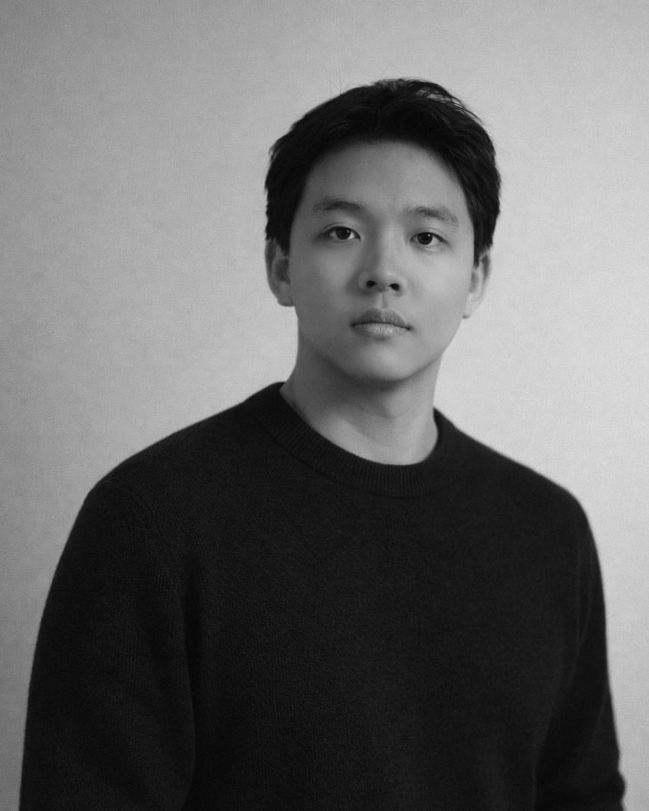 Black and white portrait of a young Asian man with short dark hair, wearing a black sweater, looking directly at the camera with a neutral expression.