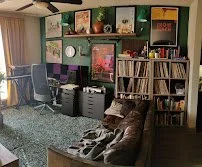 Living room with a television, bookshelf filled with books, and a sitting area with a couch and a chair.