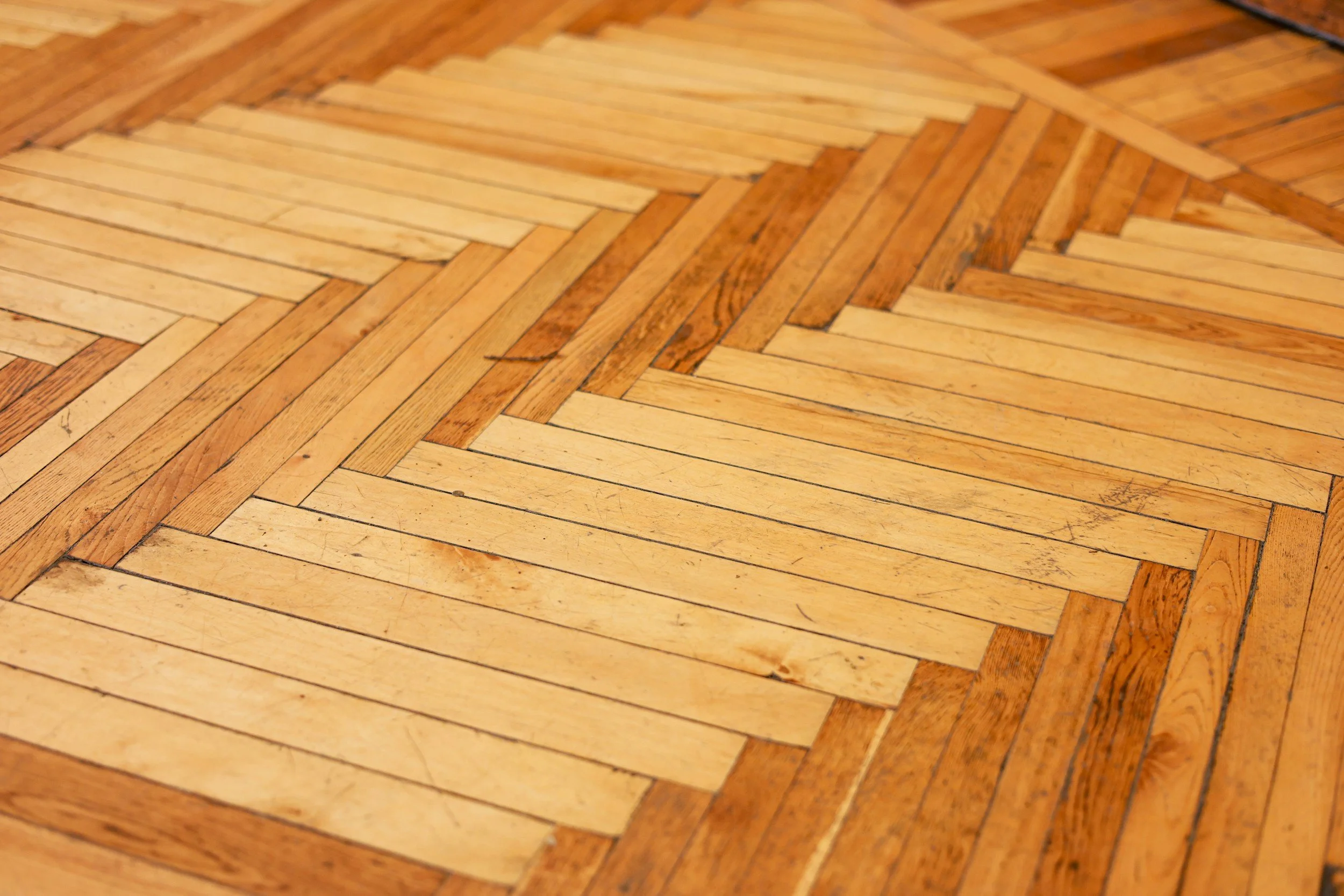Close-up of a wooden floor with light and dark wood planks arranged in a herringbone pattern.
