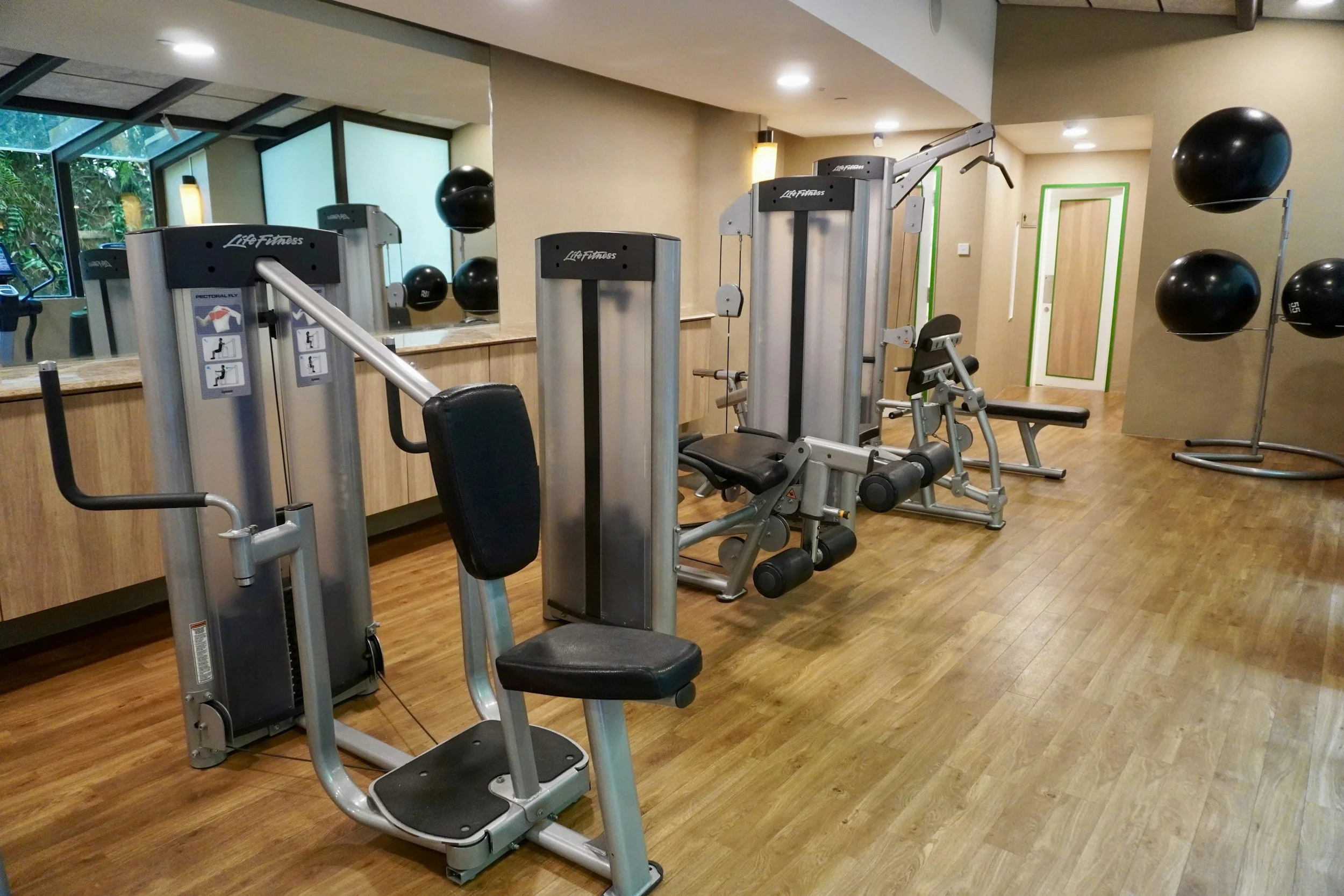 An indoor gym with exercise machines, black medicine balls, and a wooden floor.