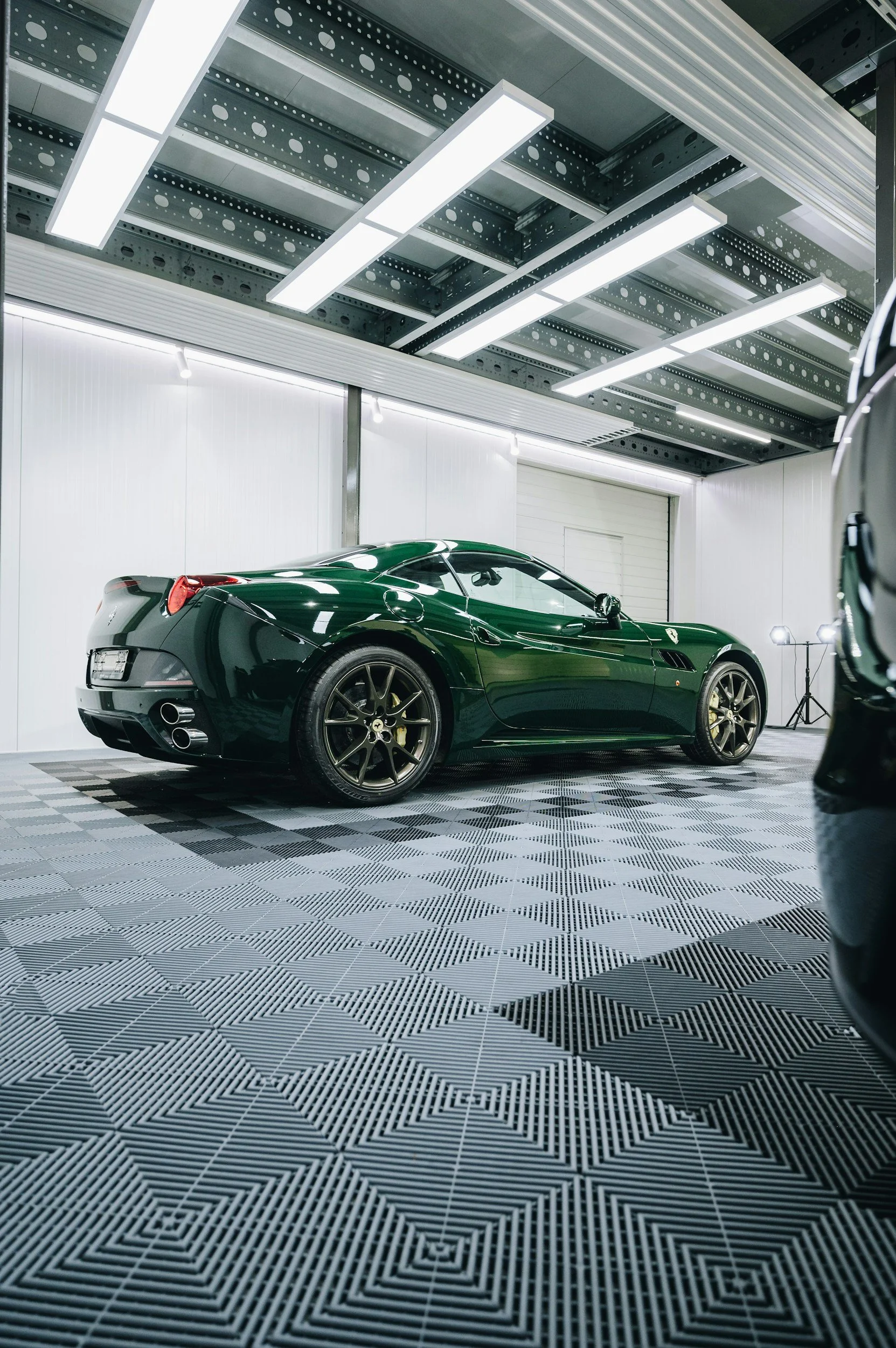 A black sports car, possibly a Ferrari, parked inside a well-lit garage with a distinctive patterned floor.