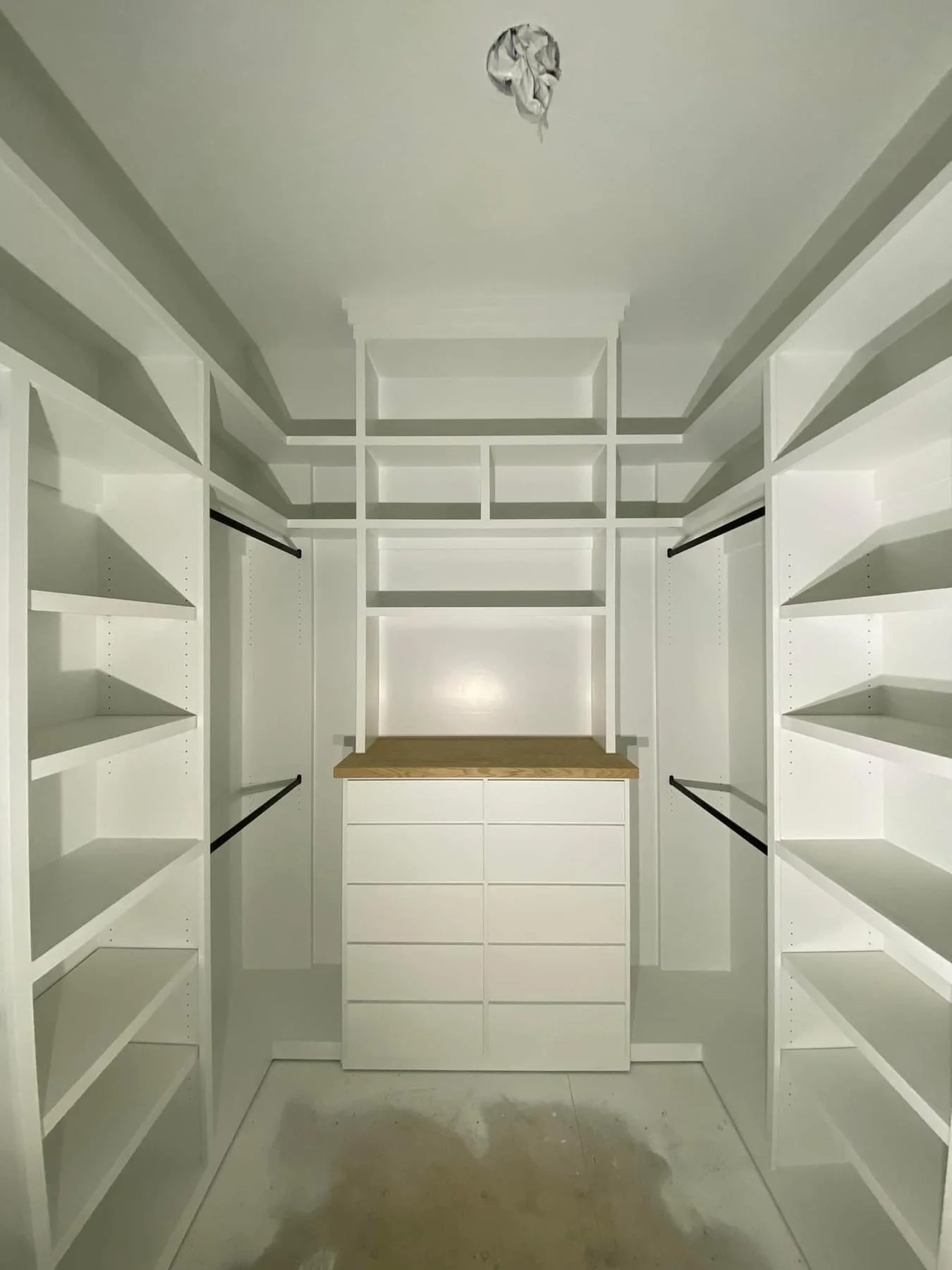 Empty walk-in closet with white built-in shelves and a wooden countertop at the back.