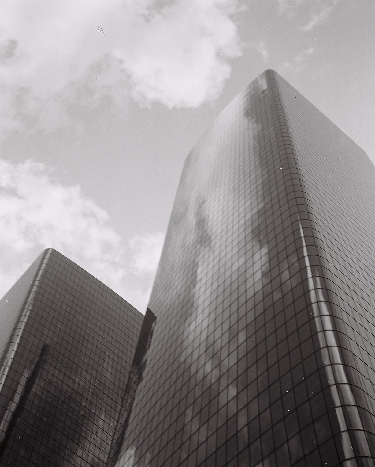 A black and white photo of a modern skyscraper with a curved glass facade, reflecting the clouds and sky above.