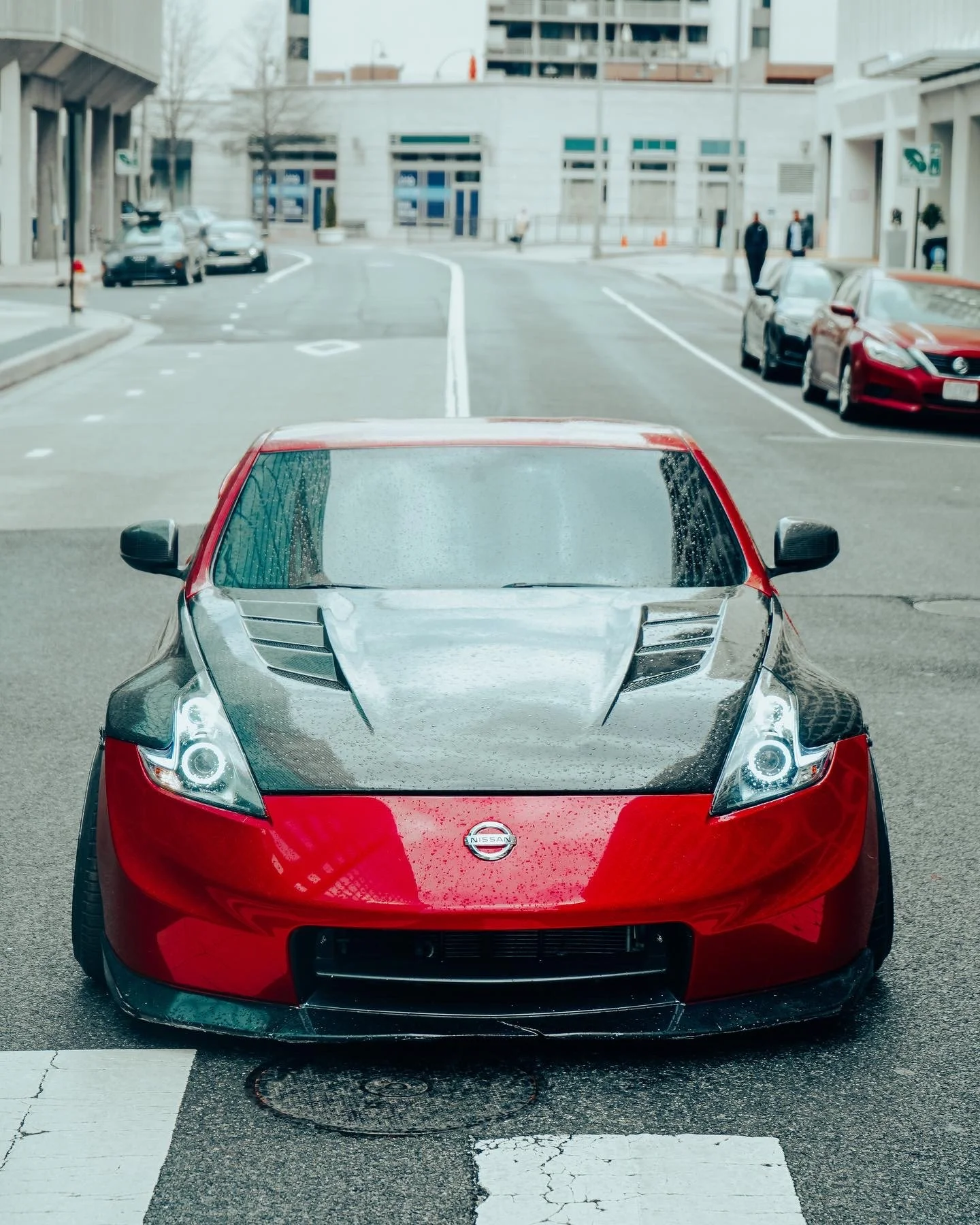 Red Nissan sports car parked in a city street, front view with the building in the background.