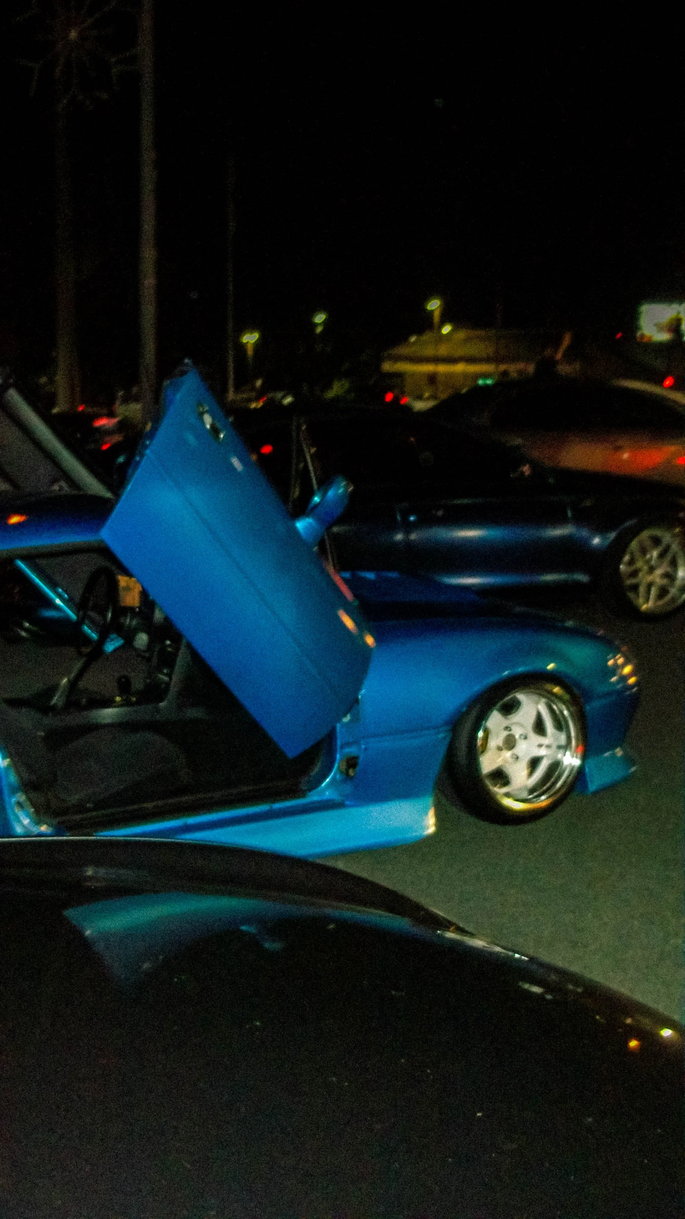 A blue sports car with its driver-side door open in a parking lot at night.