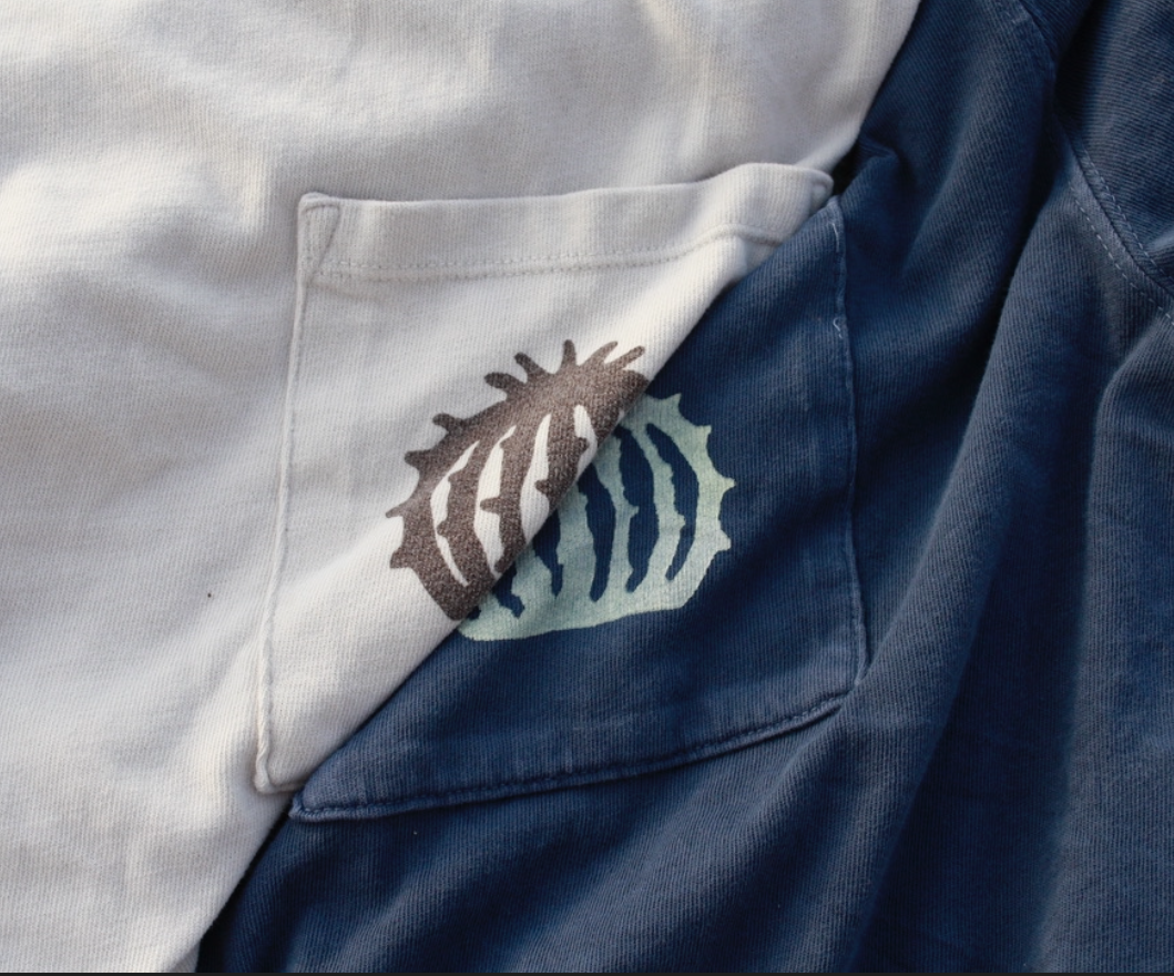 Close-up of two overlapping shirts, one white and one blue, with a logo featuring a stylized fish on the pocket of the white shirt.