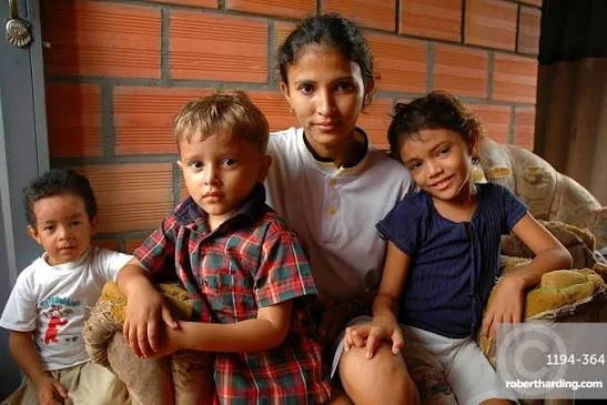 Four children sitting together indoors with a brick wall background, posing for the camera.