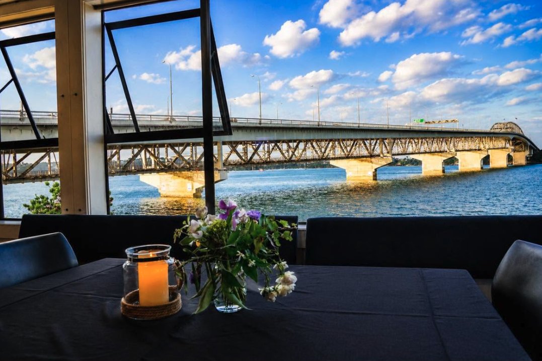 Royal New Zealand Yacht Squadron  - View of a bridge over a body of water, seen from inside a room with a table, a candle, and flowers in a vase.