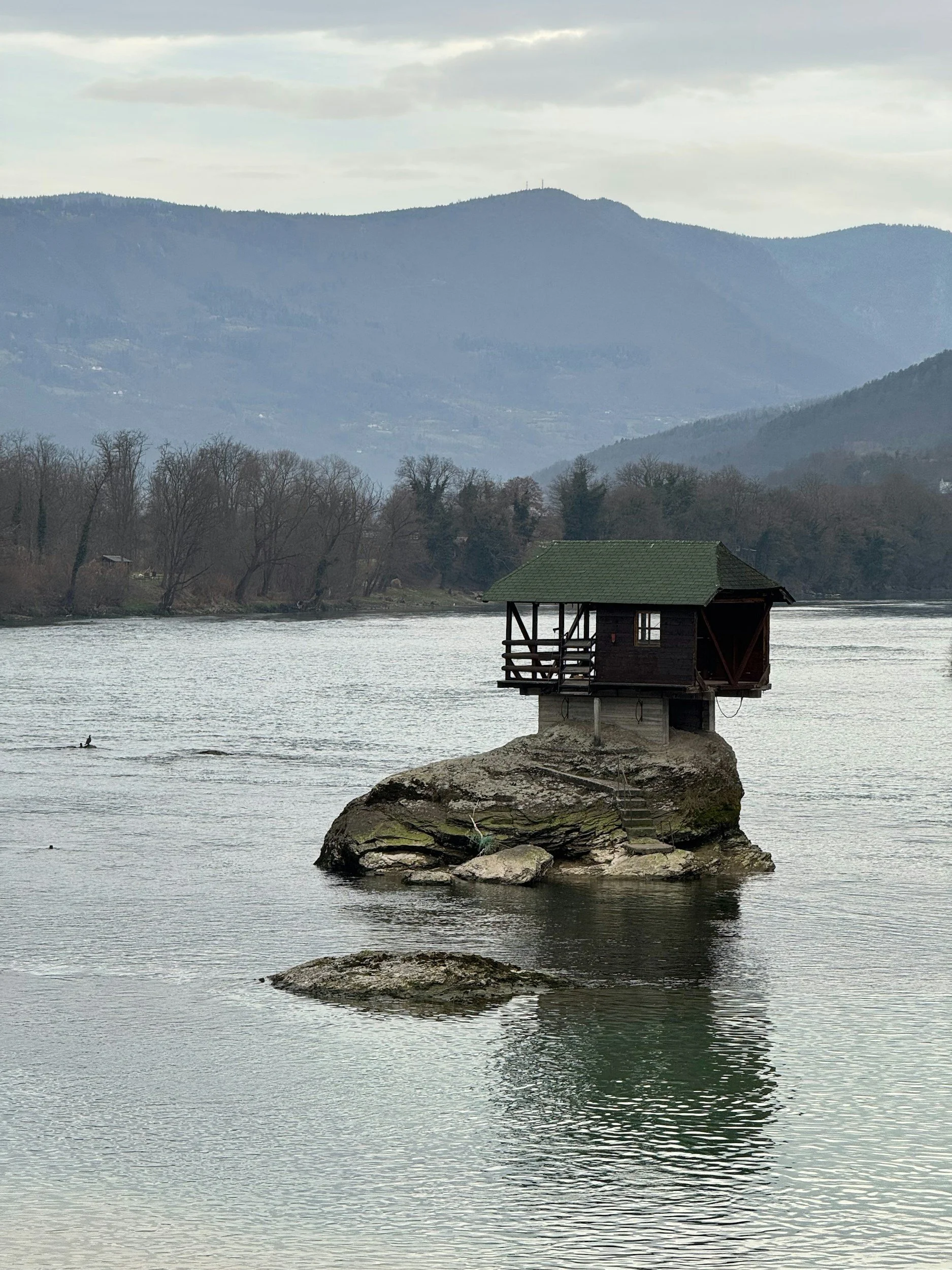 Small wooden house with a green roof on a rock in a calm river