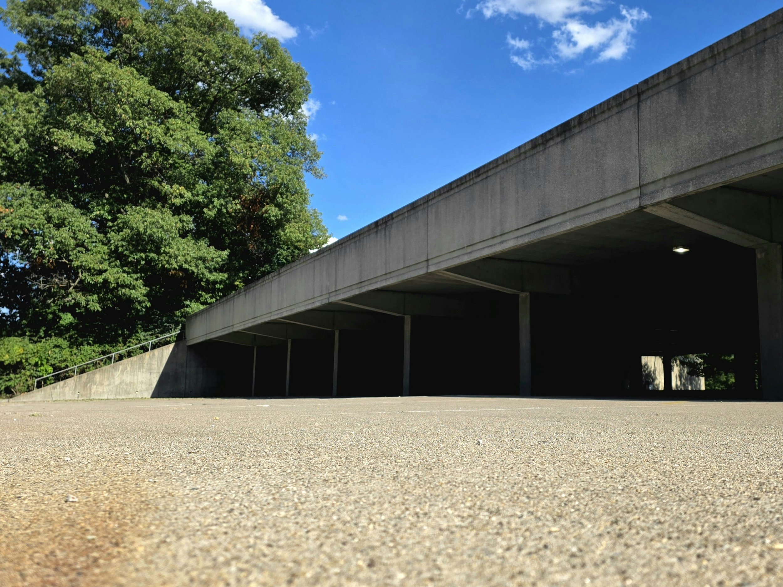 Low-angle view of a concrete structure with a large tree and blue sky in the background.