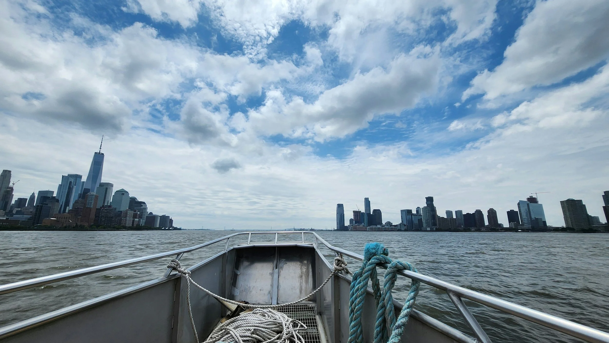 View of the New York City skyline from a boat on the water, with clouds in the sky.