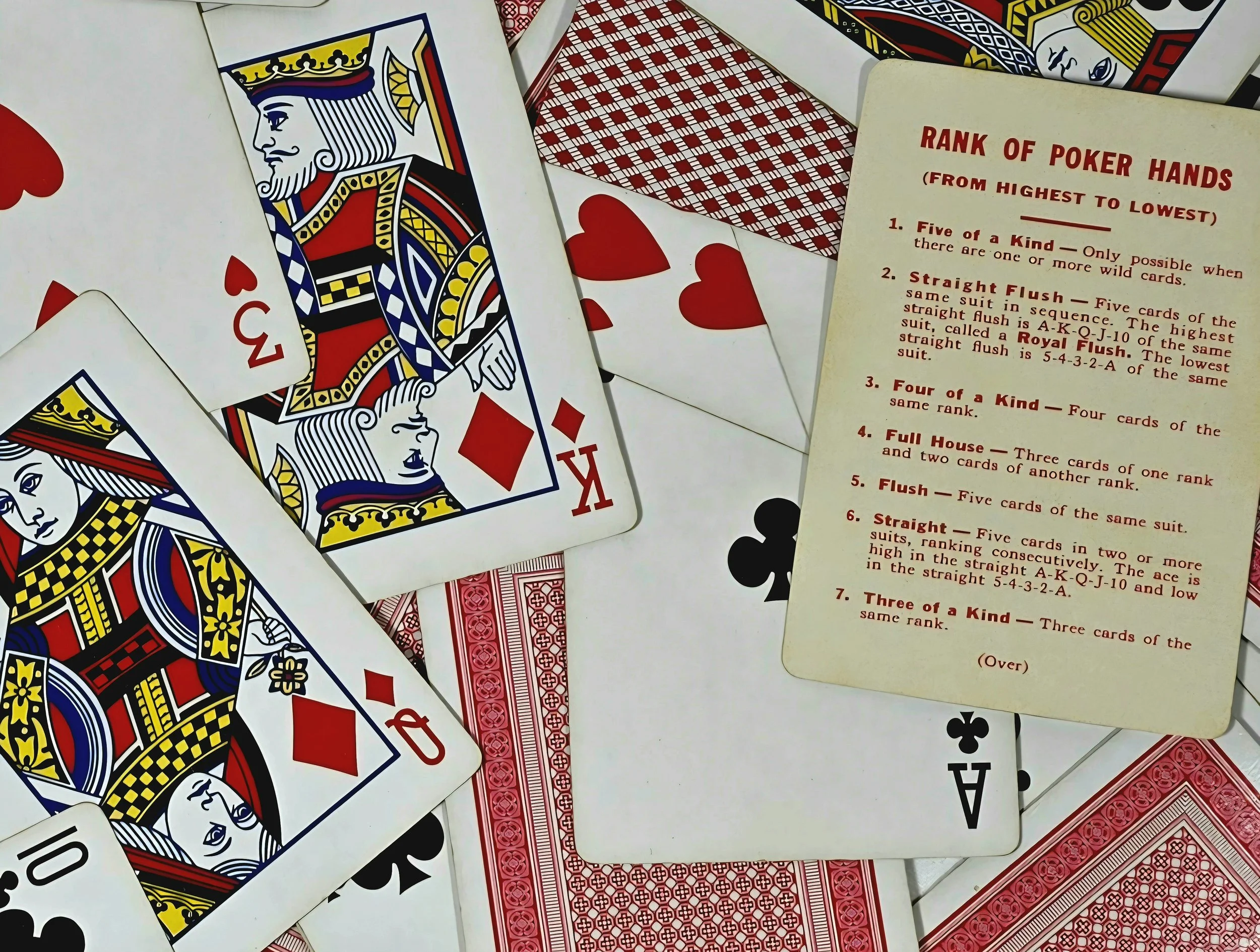 A scattered collection of playing cards, primarily featuring a queen of hearts, along with an informational card about poker hands.