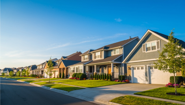 A row of suburban houses with well-maintained lawns under a clear blue sky.