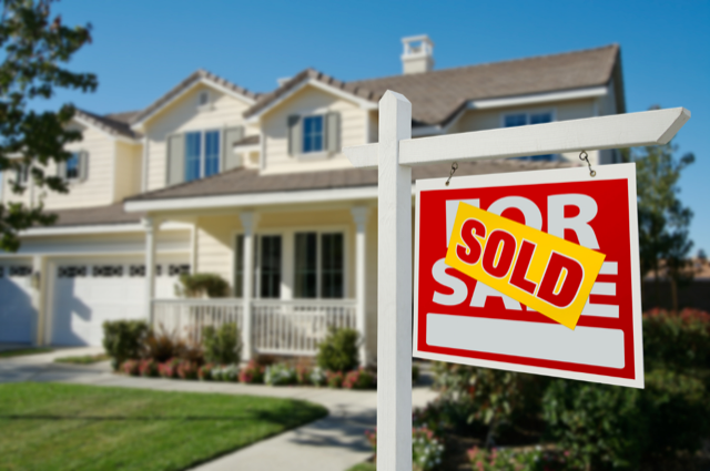 Real estate sign in front of a house with a "Sold" overlay.