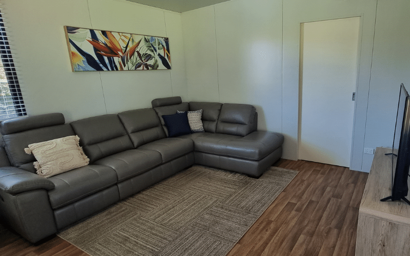 Living room with a dark gray sectional sofa, decorative pillows, a colorful artwork on the wall, a wooden floor, and a TV on a stand.