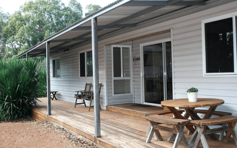 Wooden outdoor porch with table and benches in front of house with sliding glass door and windows