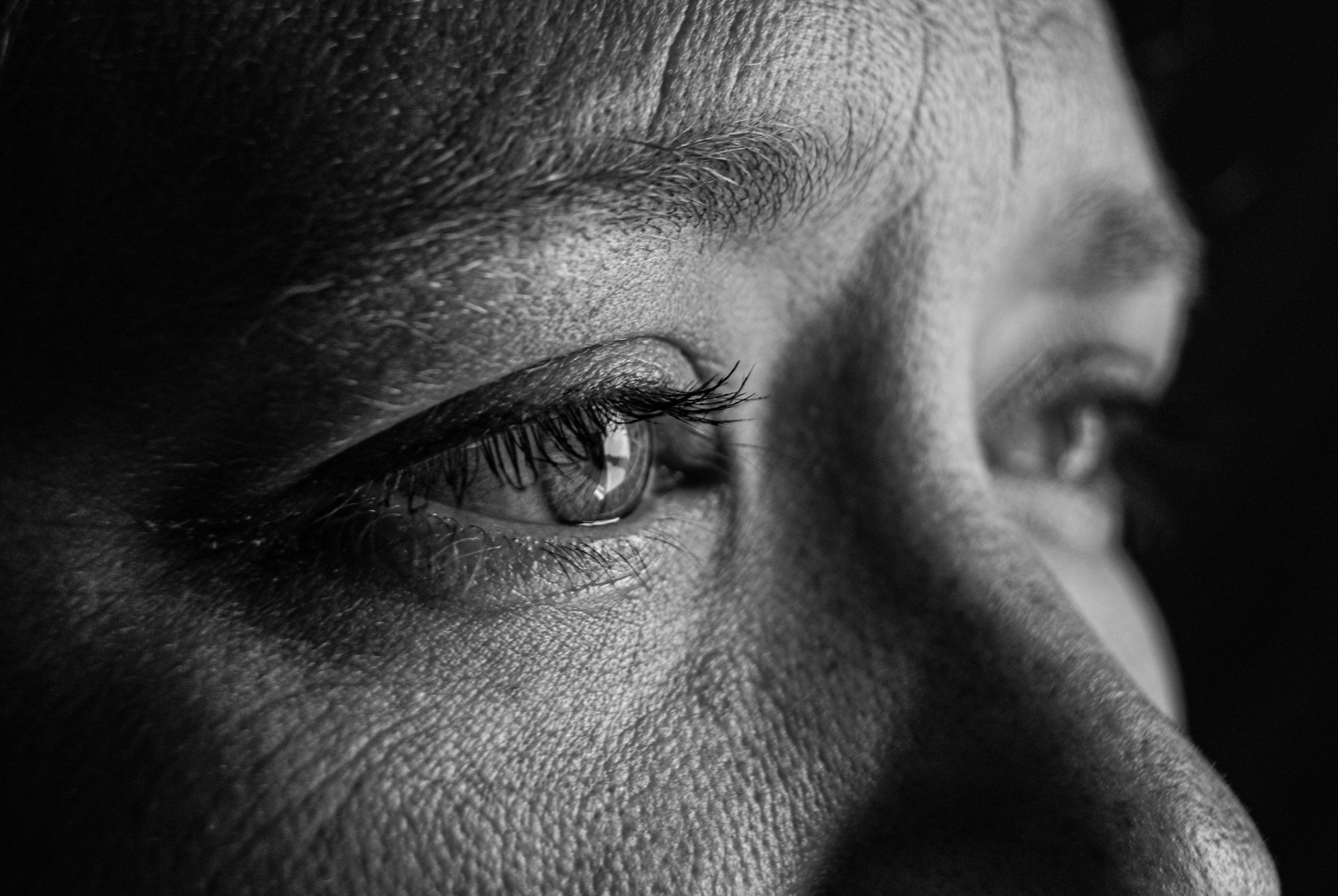 Close-up black and white photograph of a person's face, focusing on closed eye, eyebrow, and surrounding skin texture.