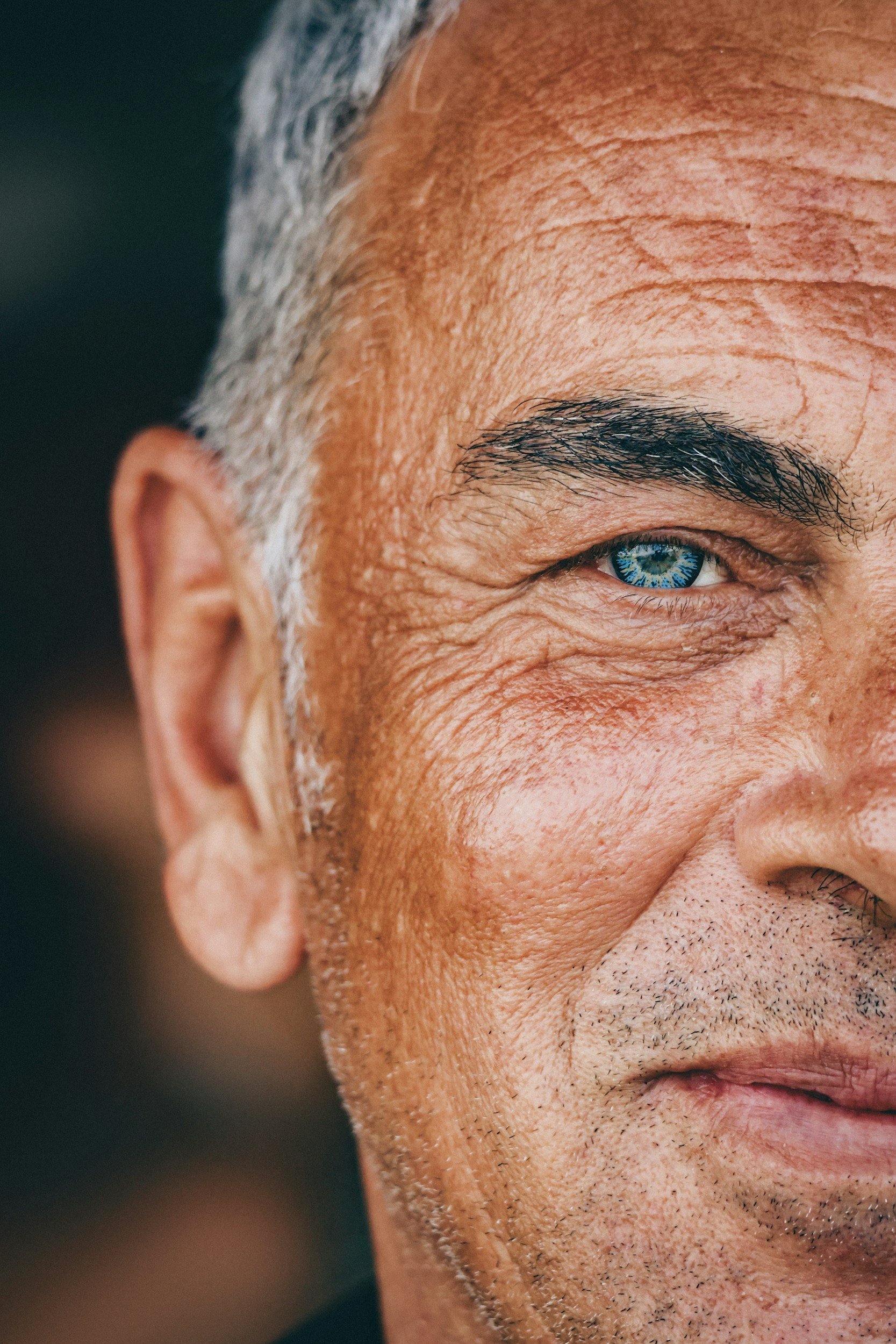 Close-up of a smiling senior man's face, showing his right eye, part of his mouth, ear, and wrinkles.
