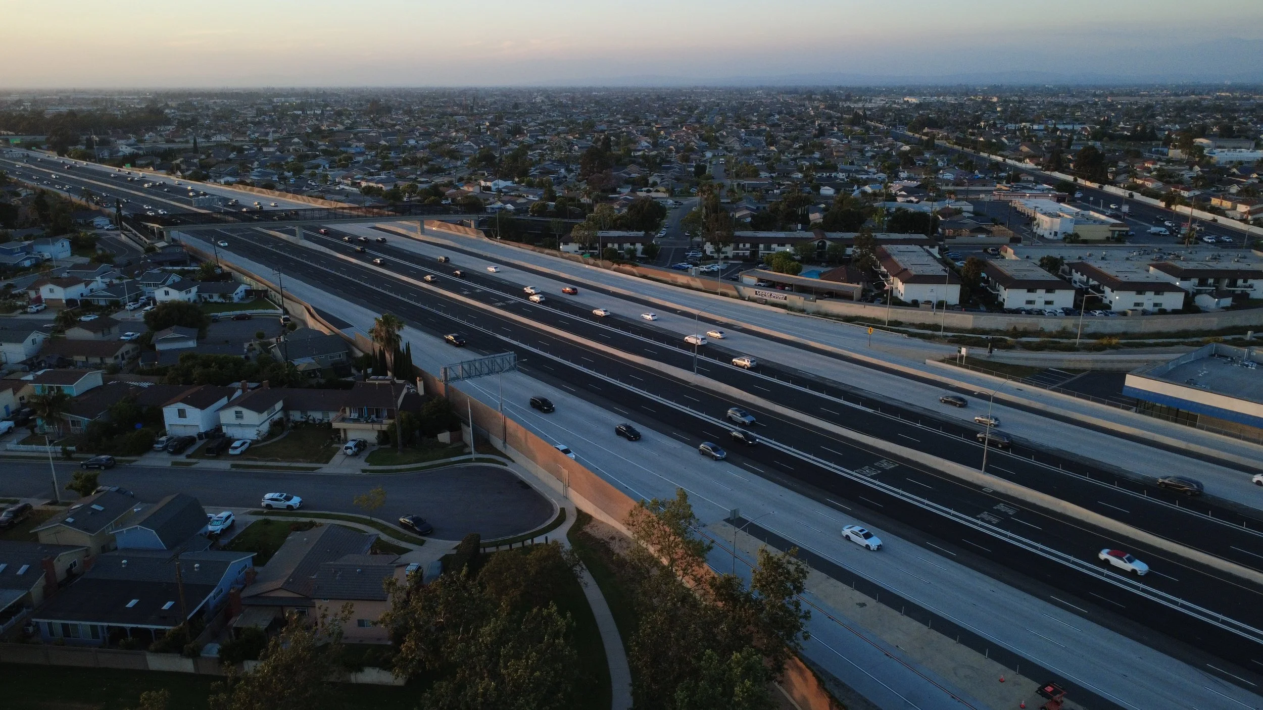An aerial view of a highway overpass with cars traveling on multiple lanes, surrounded by residential neighborhoods in a cityscape, during twilight.