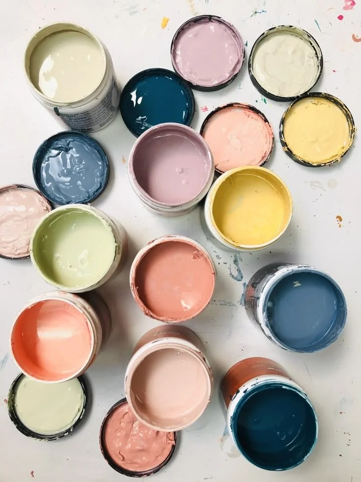 Multiple open paint cans with pastel and bright colors on a white surface.