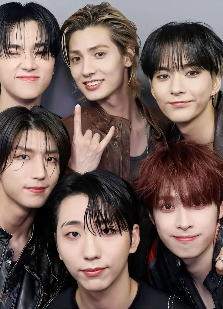 Group of six young men taking a close-up selfie, some smiling and making gestures, with a gray background.