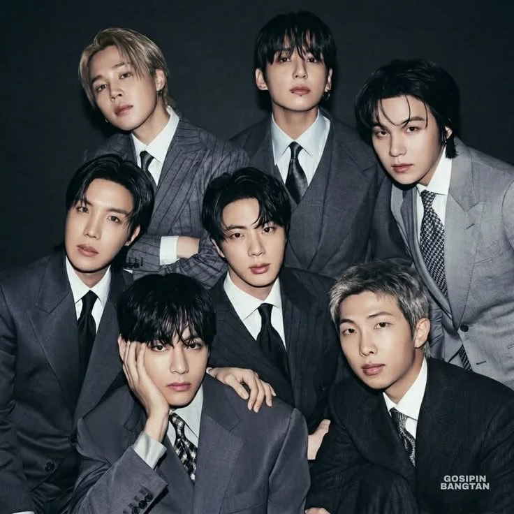 Seven young men dressed in formal suits posing together against a dark background.
