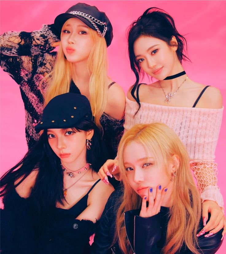 Four young women posing together against a pink background, dressed in trendy outfits with accessories, showcasing a fashionable, vibrant style.