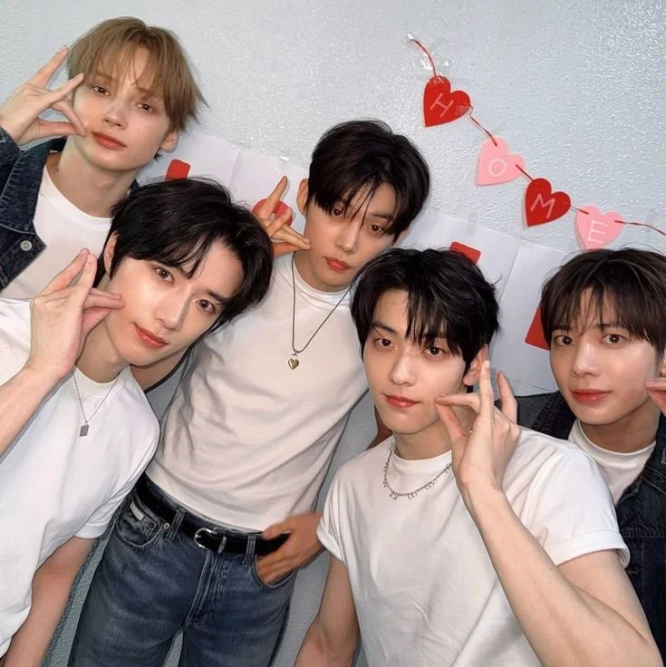 Five young men posing together in front of a Valentine's Day decoration with red and pink hearts that spell out "LOVE" and "HAVE".