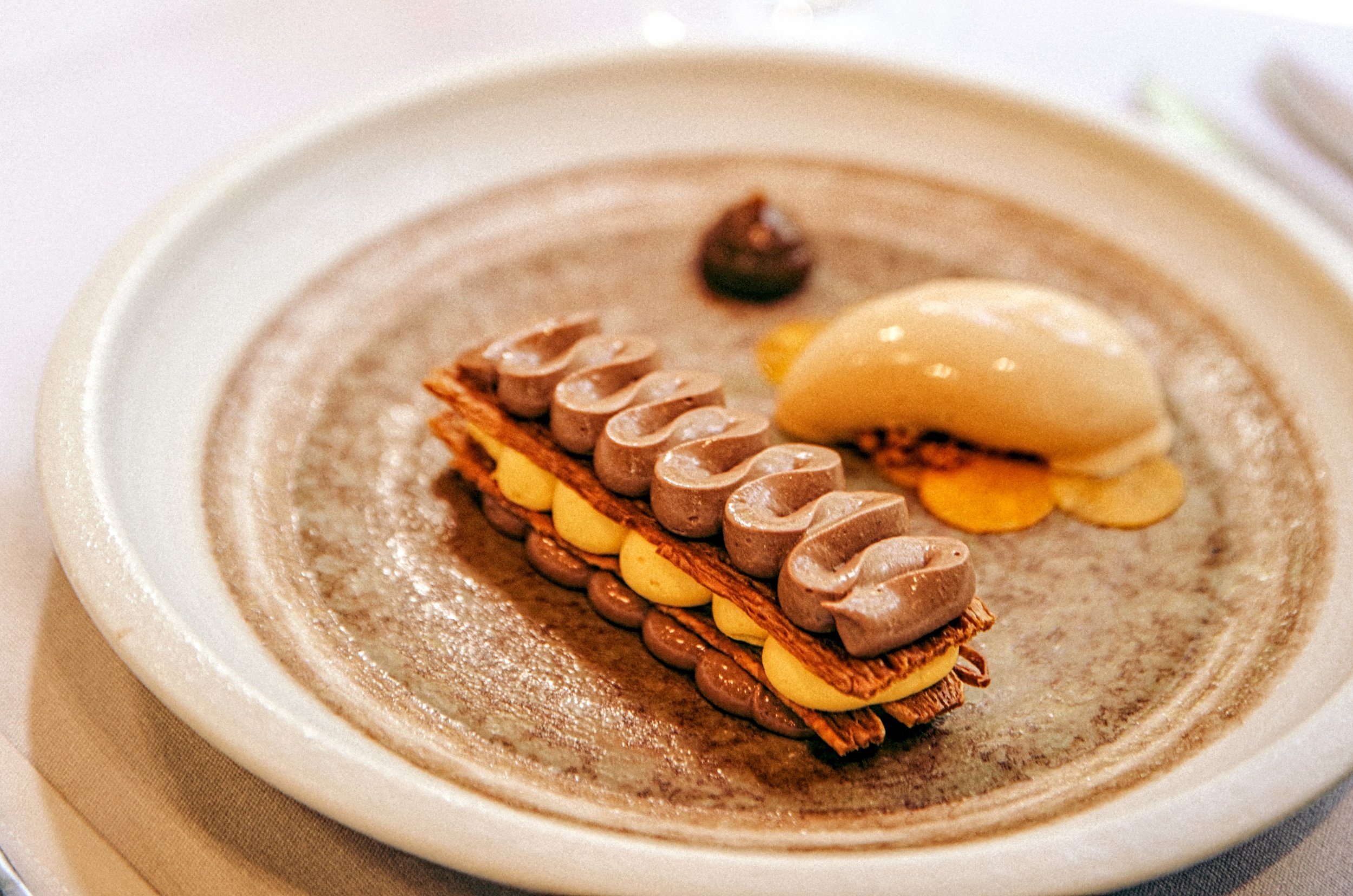 A dessert with layers of caramelia chocolate cremeux, puff pastry, pumpkin & white chocolate whipped ganache, sweet pickled squash, coffee vinegar gel and a pain d'epices ice cream
