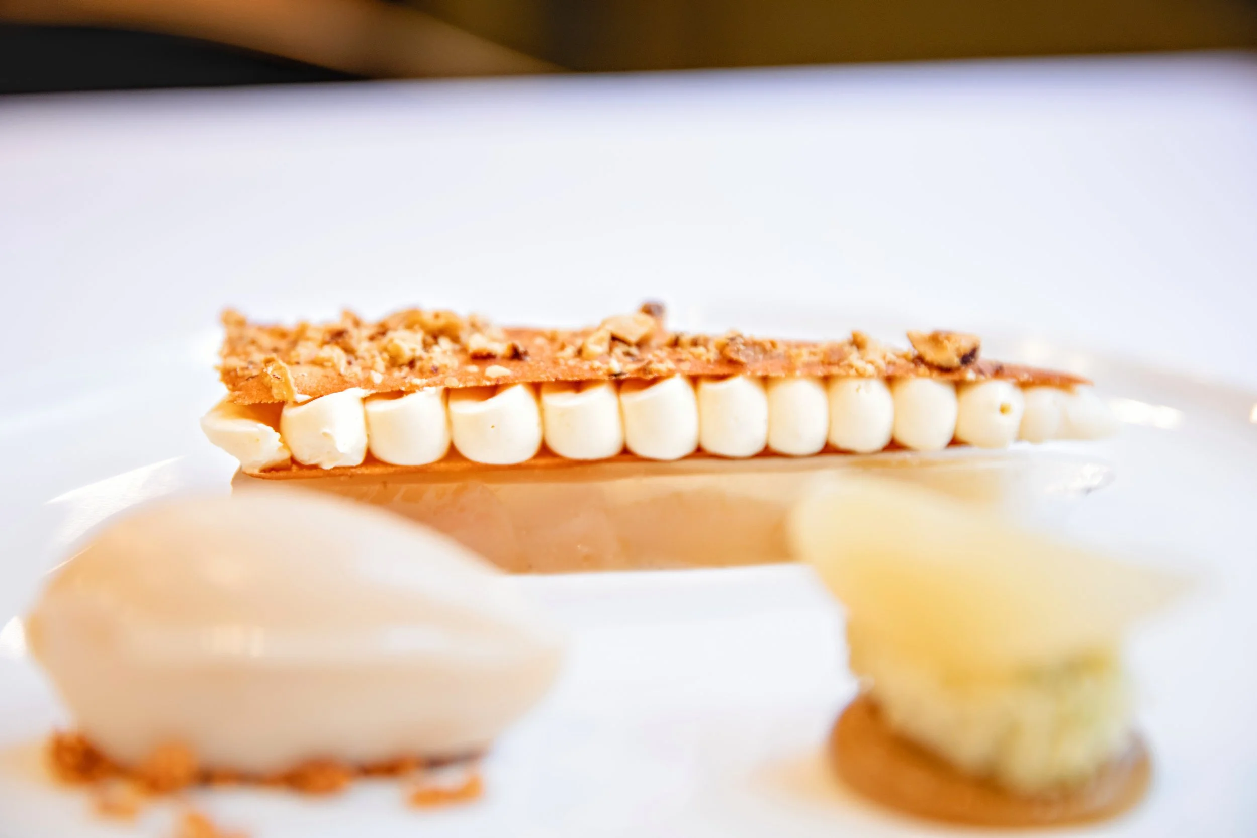 Close-up of a layered dessert of set poached pears, amaretto cremeux, hazelnut tuile, roasted pear puree, pear sorbet and a rosemary sponge.