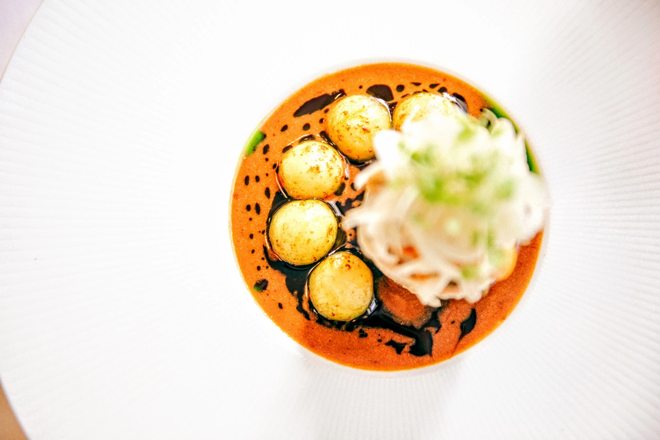 A fish dish with pomme noisette, pickled fennel & celery, scampi bisque butter sauce and garnished with microgreens on a white plate.