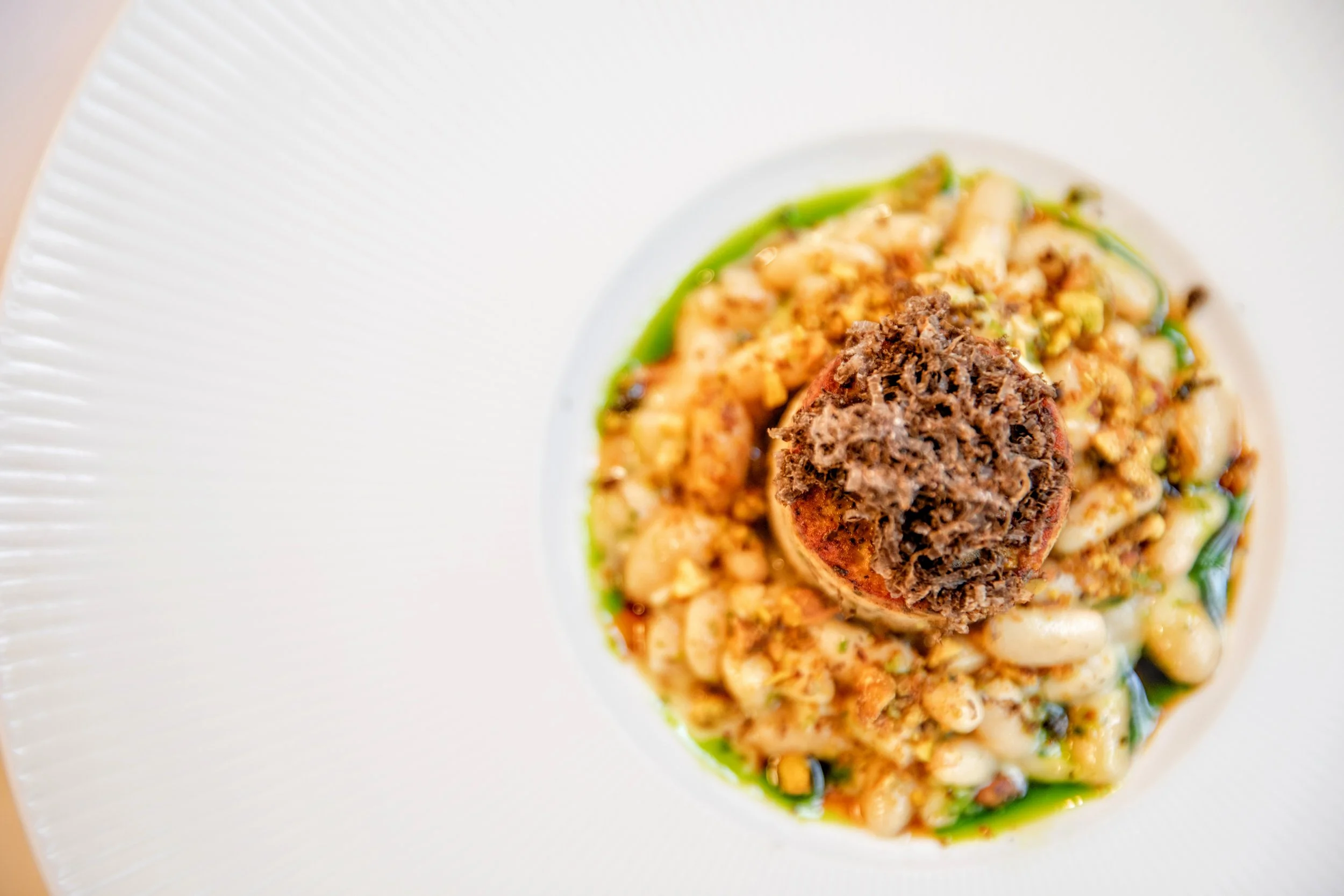 Close-up of a gourmet dish featuring a chicken boudin, coco beans, fresh winter truffle, prune puree, a chervil cream sauce, pistachio and sweetbreads.