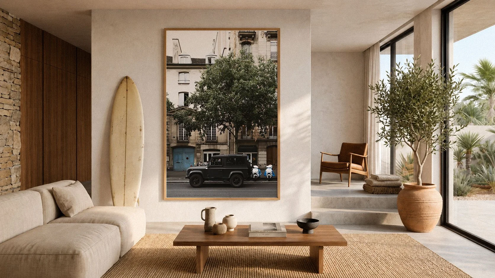 Modern living room with beige sofa, wooden coffee table, surfboard leaning against wall, large framed cityscape photograph, potted tree, armchair, and large floor-to-ceiling windows showing outdoor desert landscaping.