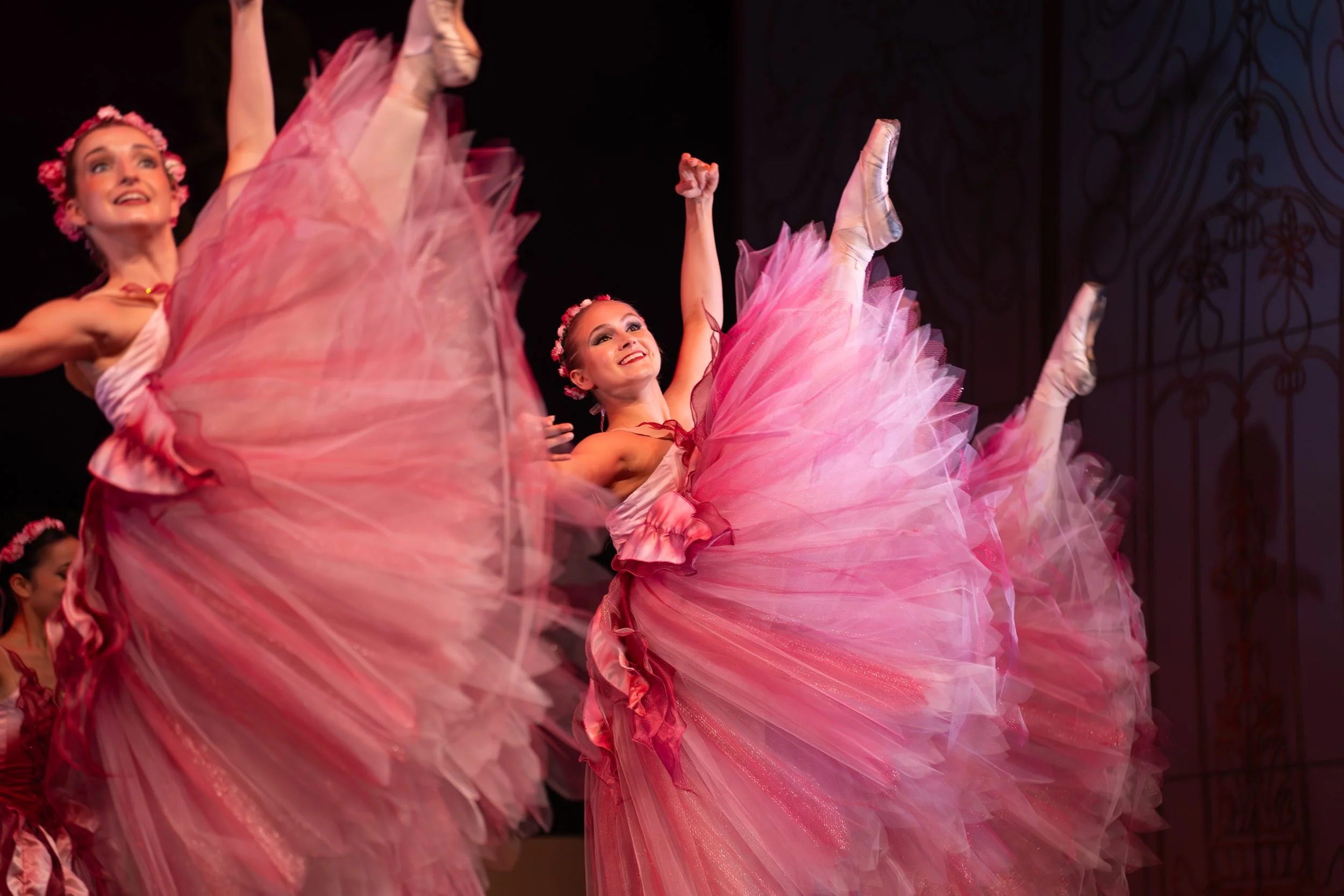 Ballet dancers in pink tutus performing on stage with dark background.