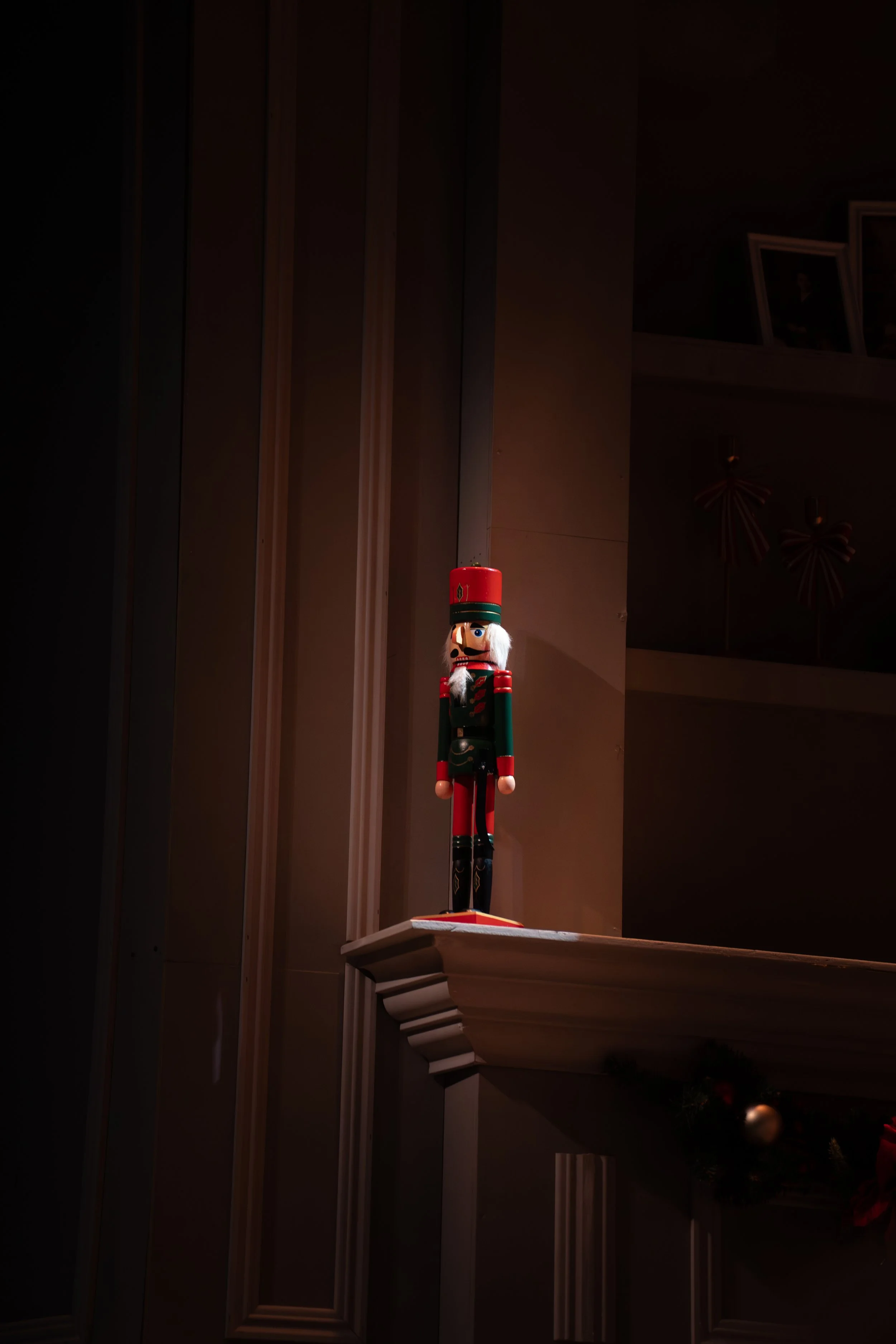 A nutcracker figurine dressed in a red and green military uniform standing on a shelf in a dimly lit room.