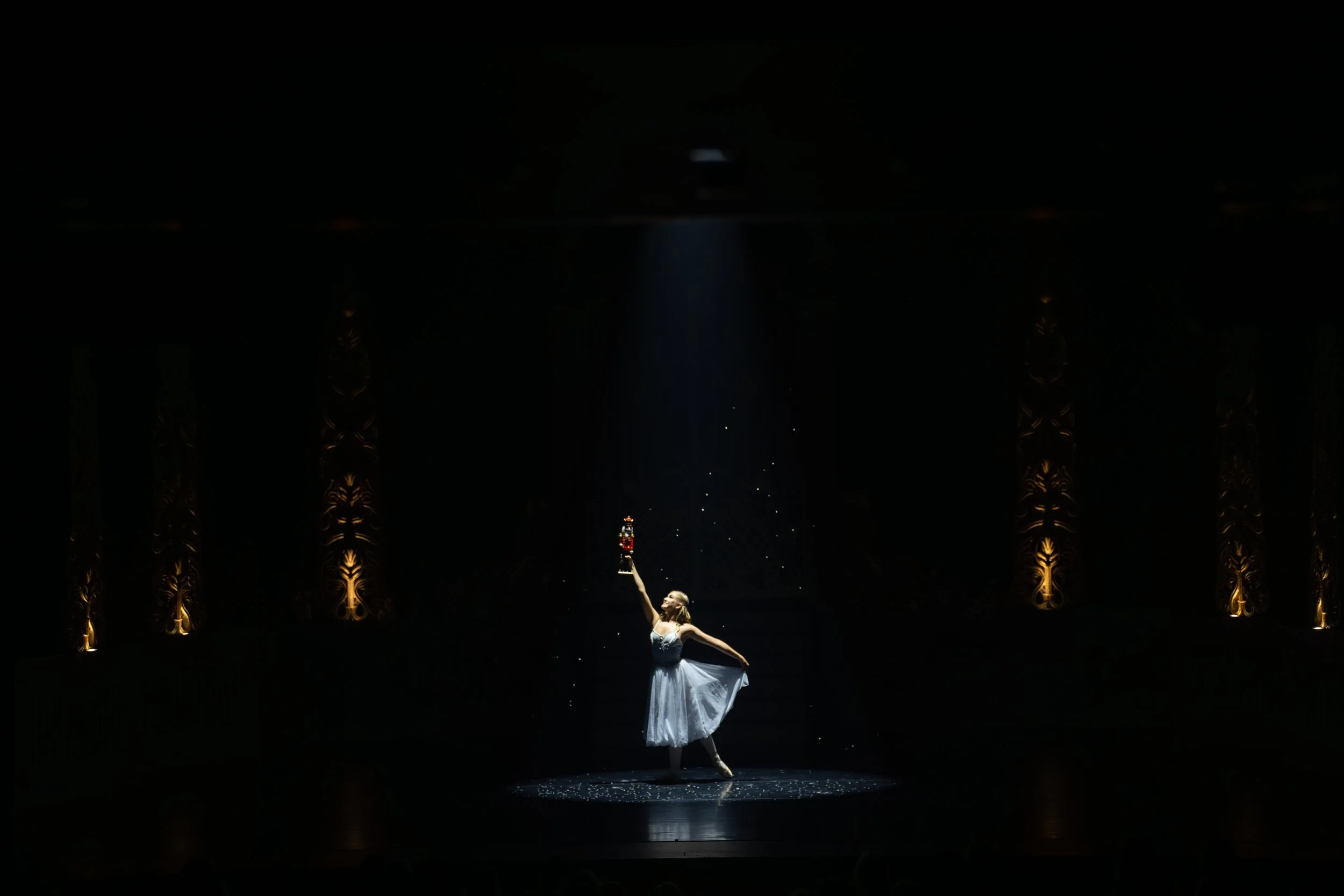 Ballet dancer on stage illuminated by a spotlight, with ornate curtains on either side.