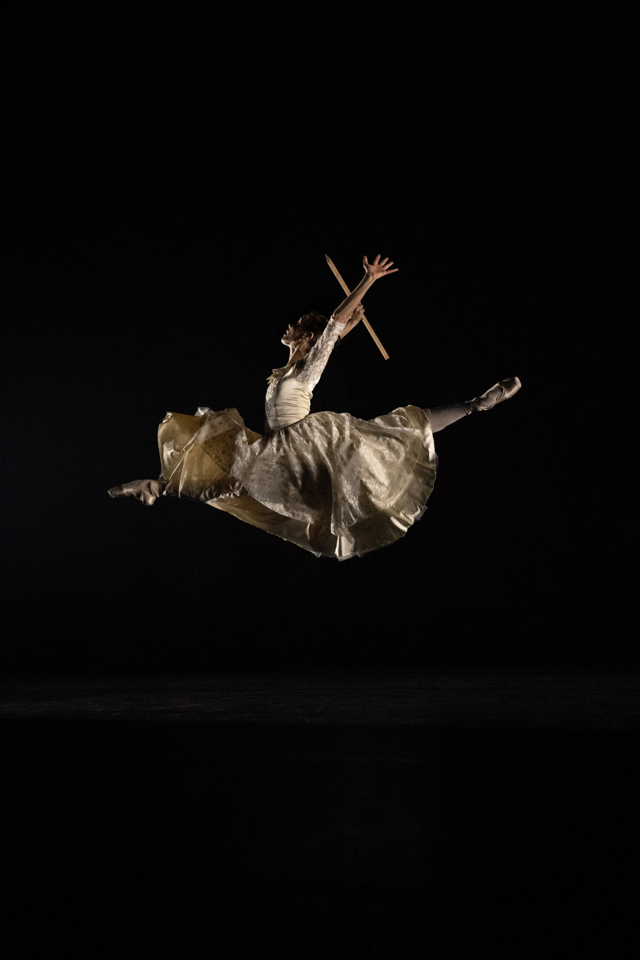 A ballet dancer in a flowing white costume performs an elegant leap against a dark background.