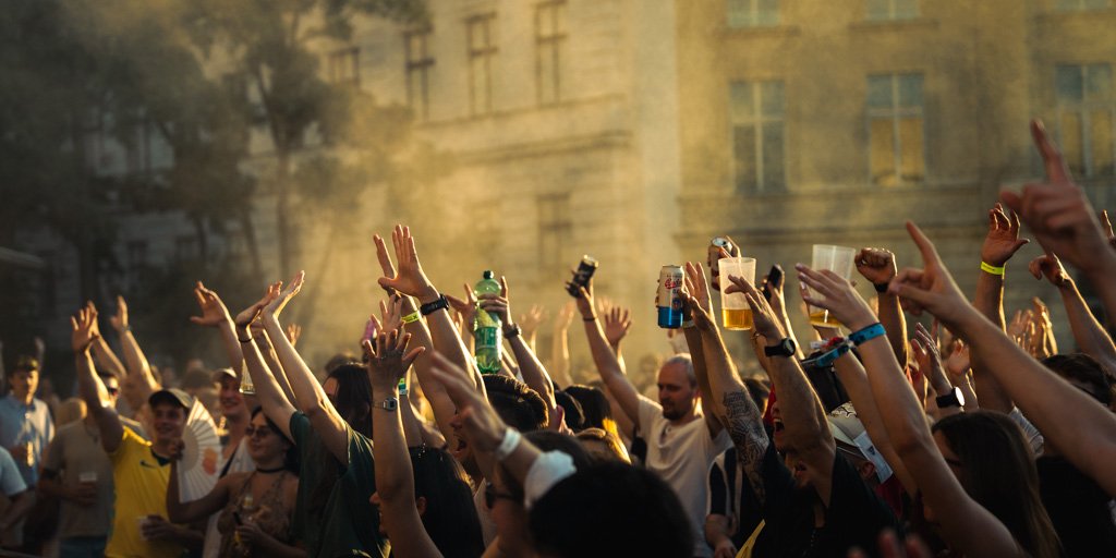 Menschen feiern mit erhobenen Armen und Getränken im Freien bei Sonnenuntergang.