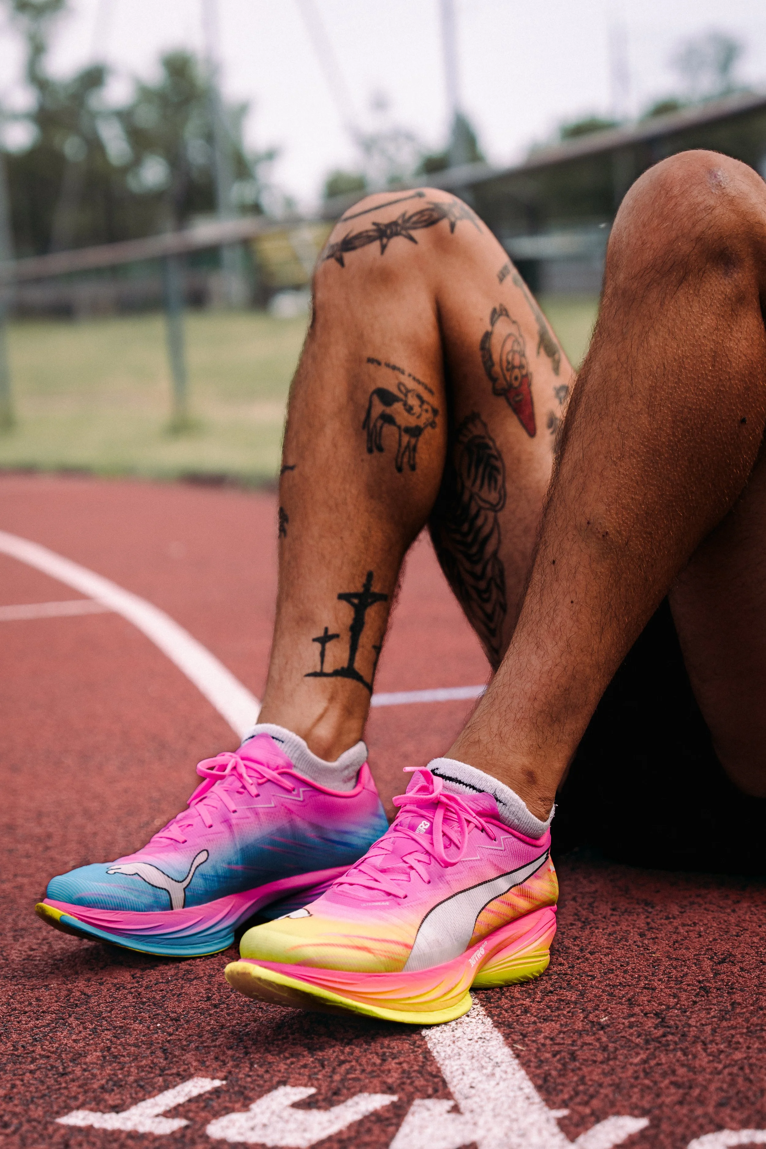 Person im Sportoutfit und pinken Laufschuhen sitzend auf einer Laufbahn.