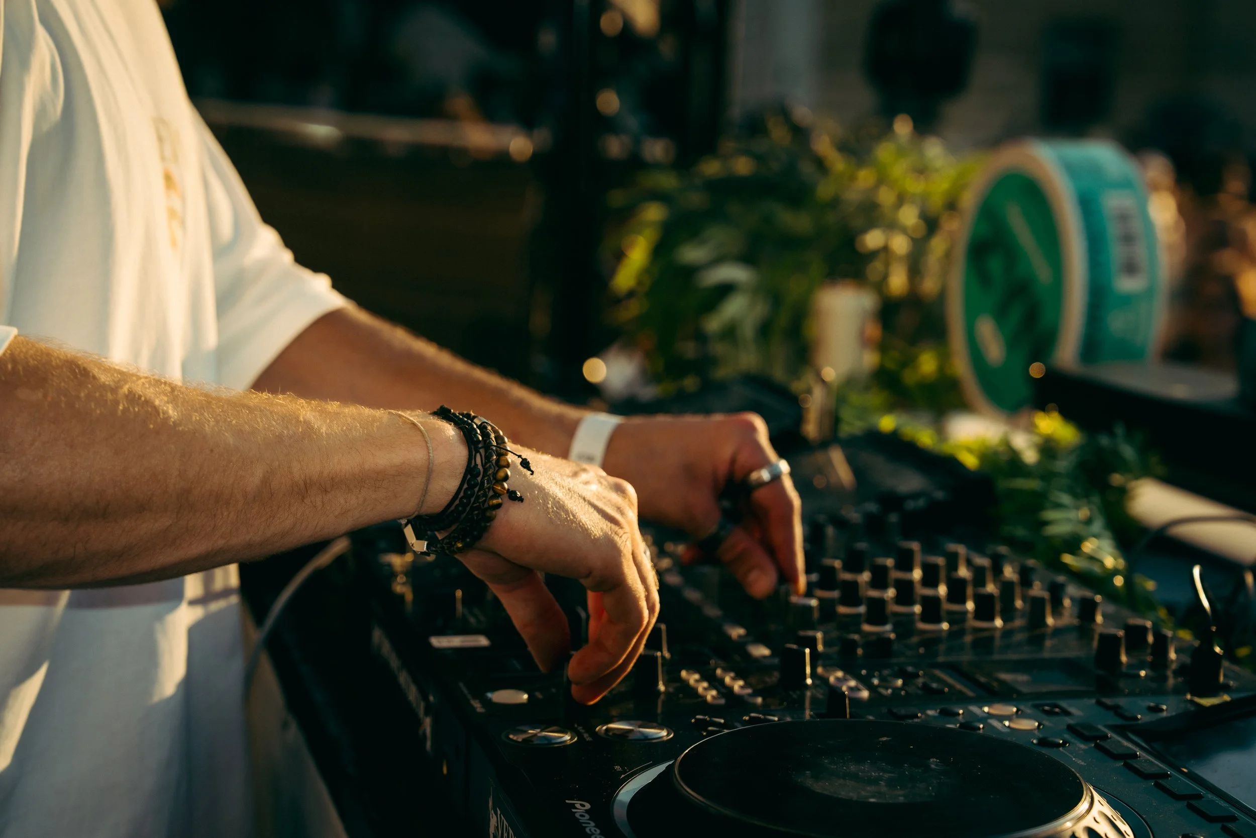 Nahaufnahme eines DJs, der mit seinen Händen an einem DJ-Mixer arbeitet, bei Sonnenuntergang im Freien.