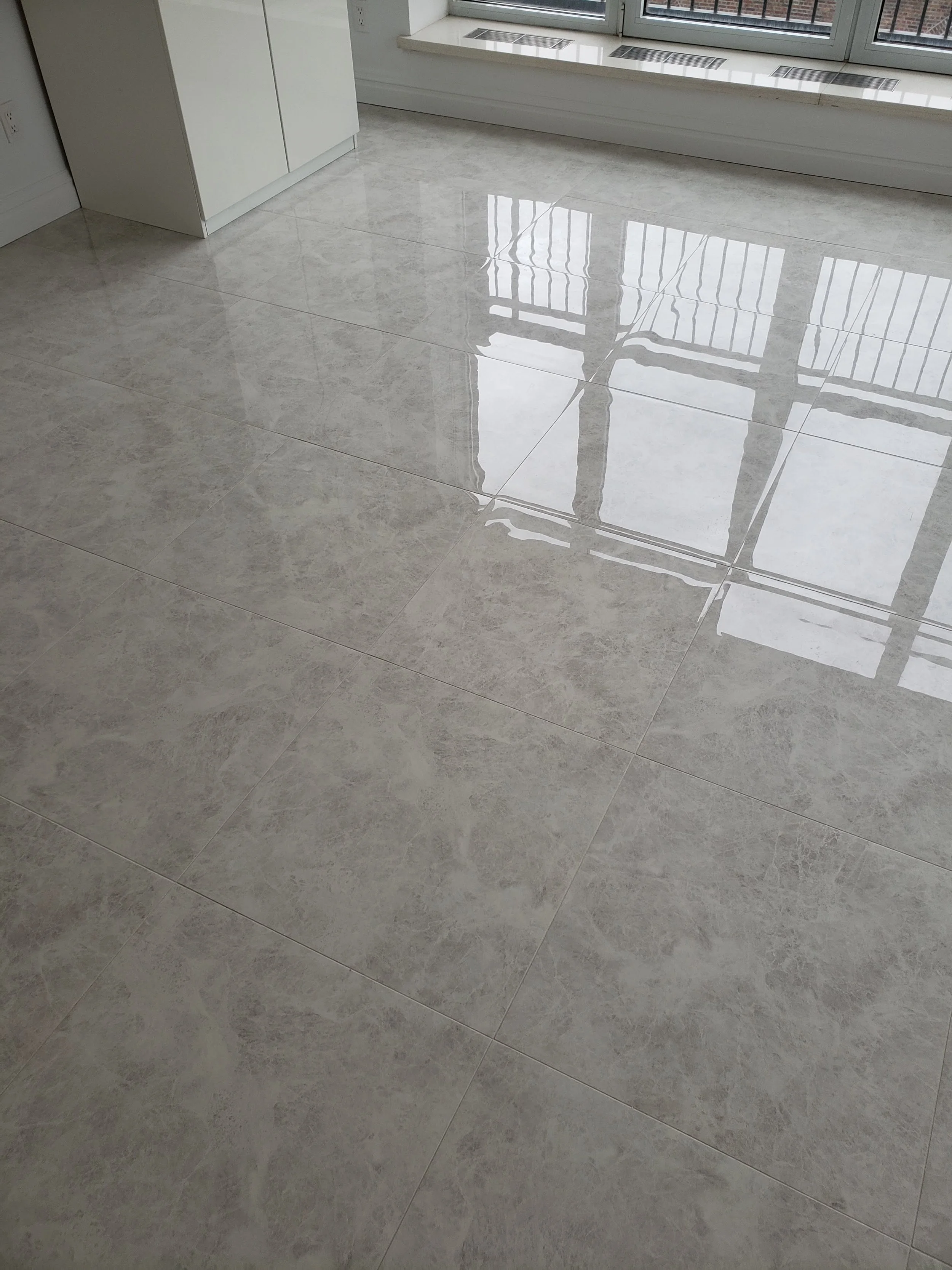Shiny beige tiled floor near a window with vertical metal bars, a white cabinet in the corner, and electrical outlets.