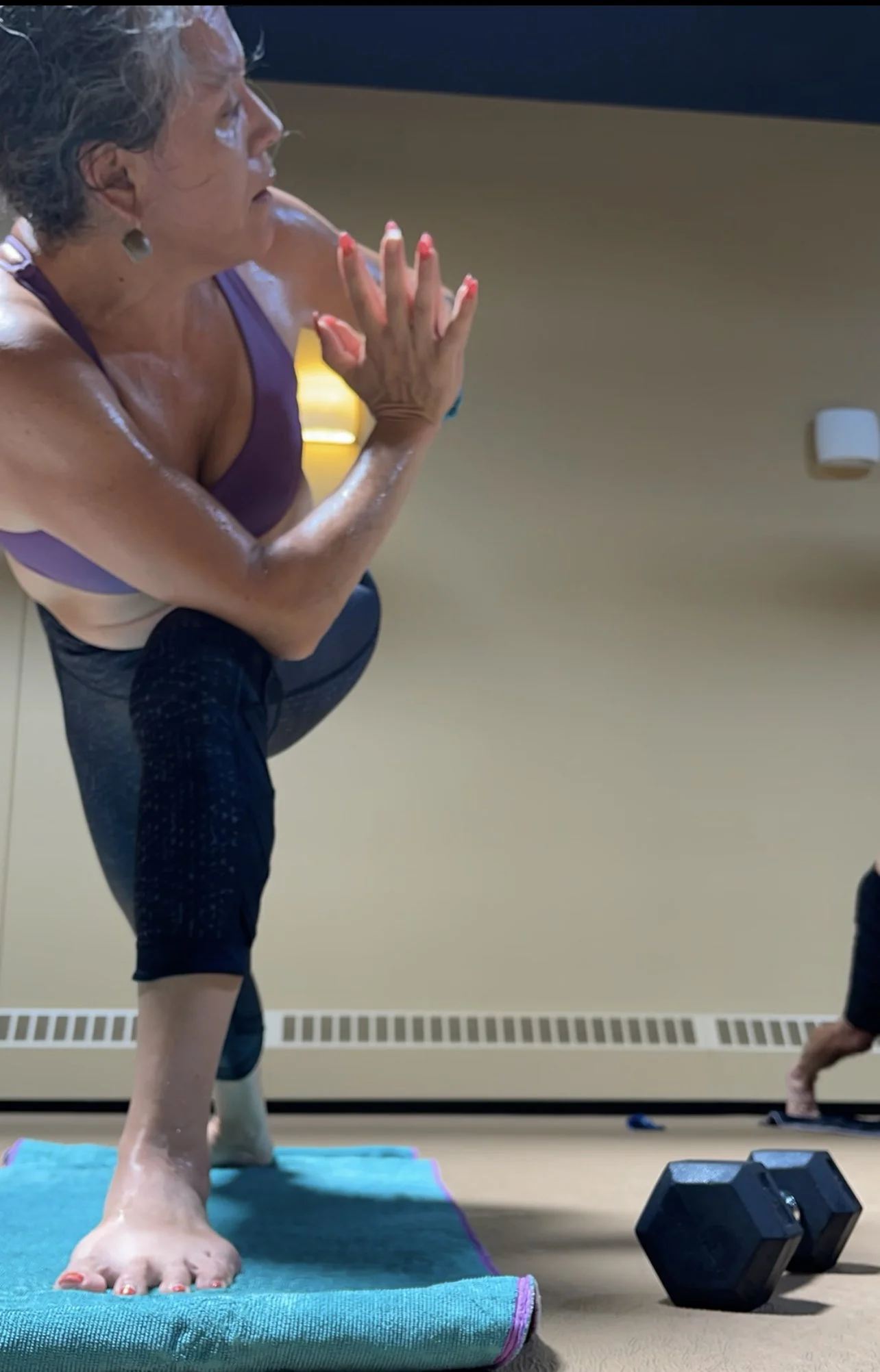 A woman in athletic wear practicing yoga or stretching on a blue mat in a room, with a fitness weight nearby.