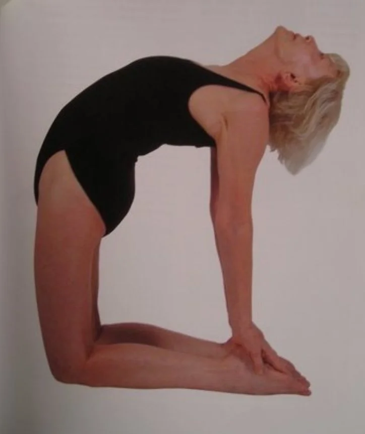 A woman is performing a yoga pose resembling a backbend with her hands and feet on the ground, and her body arched backward with her head tilted upward.