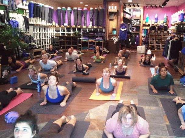 Group of people participating in a yoga or exercise class inside a retail store, with shelves of clothing and fitness equipment in the background.
