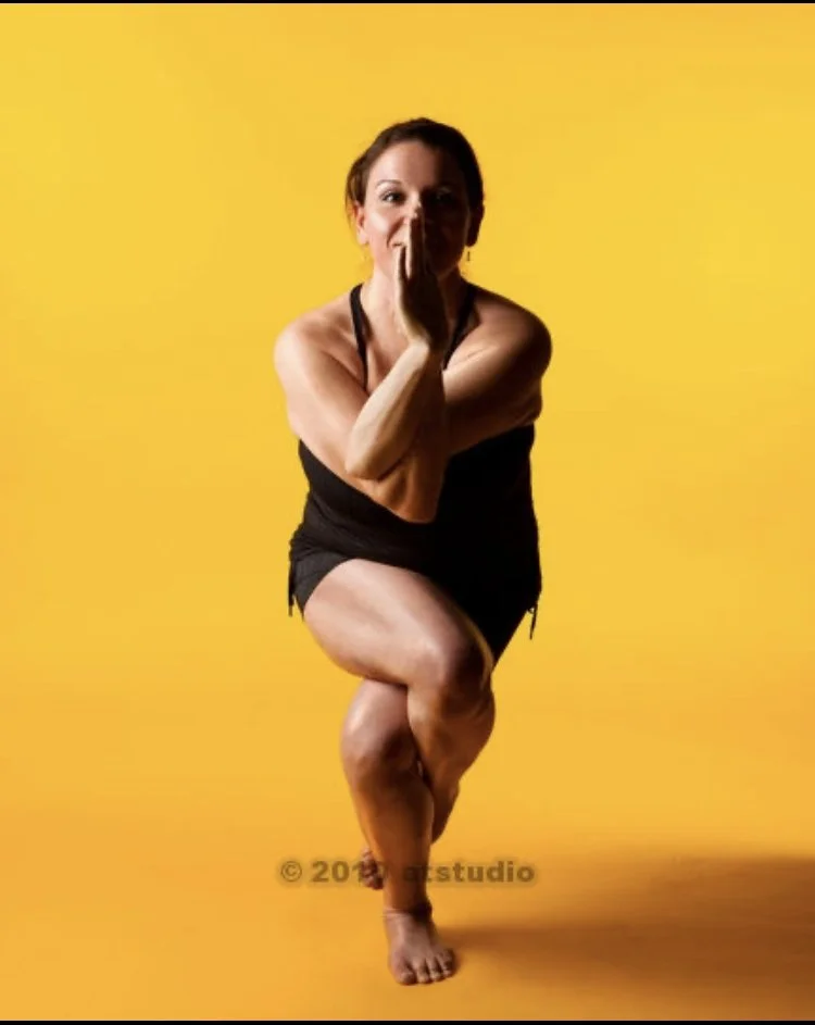 Woman performing a yoga pose on one leg against a yellow background.