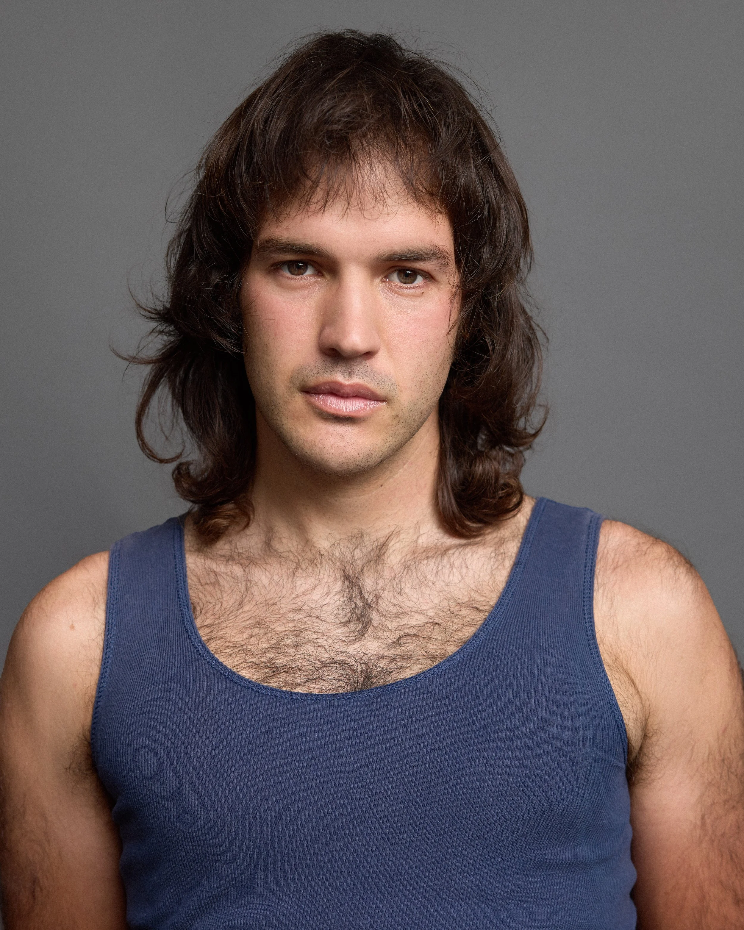 Front view of a young man with brown hair, brown eyes, wearing a blue tank top, against a gray background.